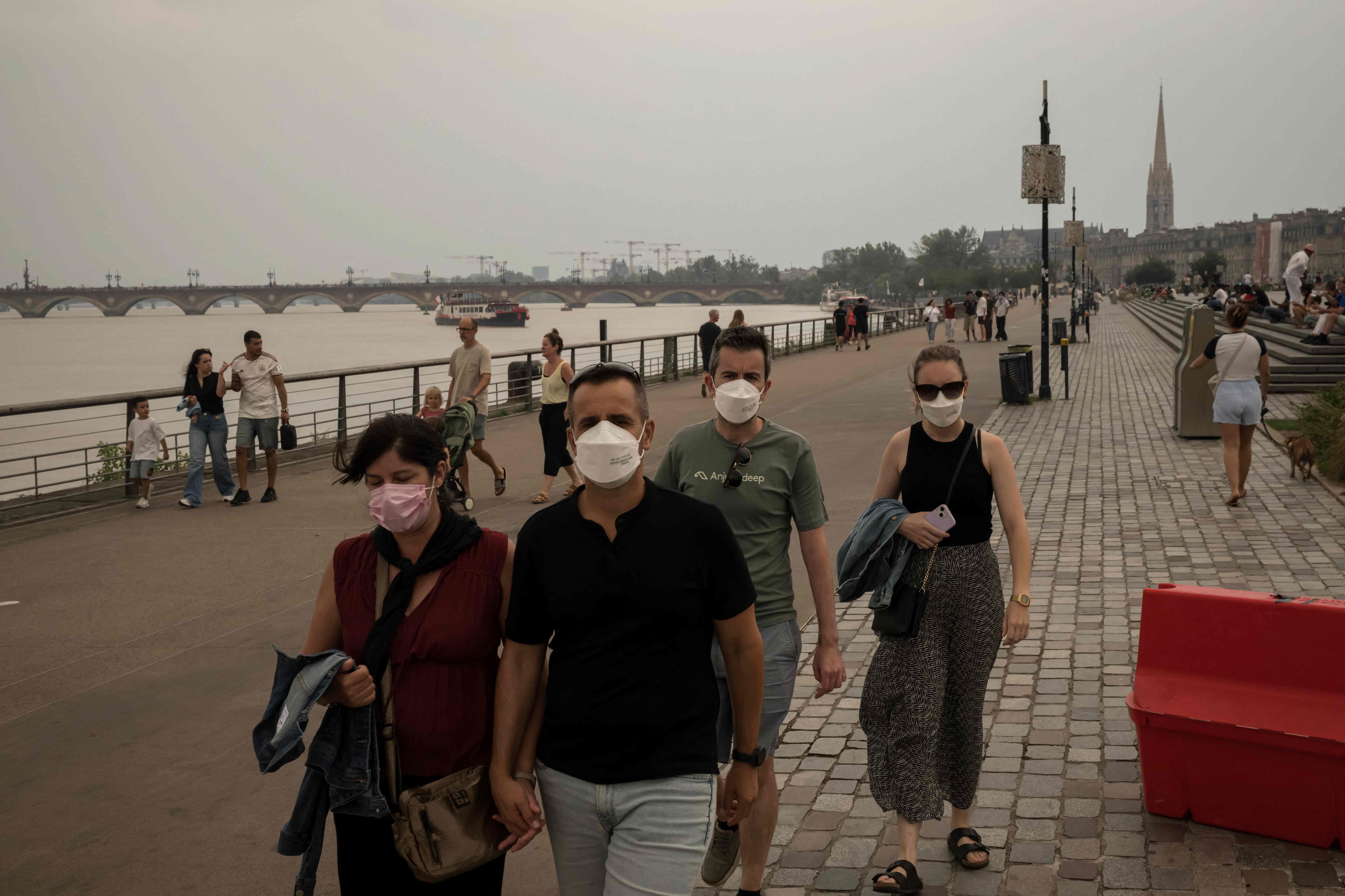 Menschen mit Masken spazieren an einem Flussufer in Bordeaux. Das Foto zeigt Rauch von nahegelegenen Waldbränden über der Stadt.