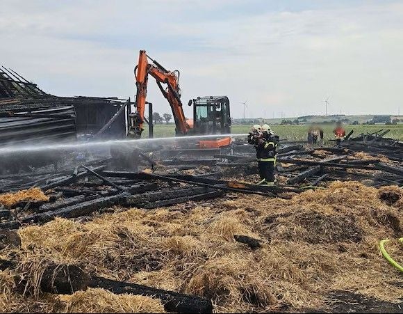 Ein Feuerwehrmann löscht Glutnester in einer abgebrannten Ruine, im Hintergrund ein Bagger.