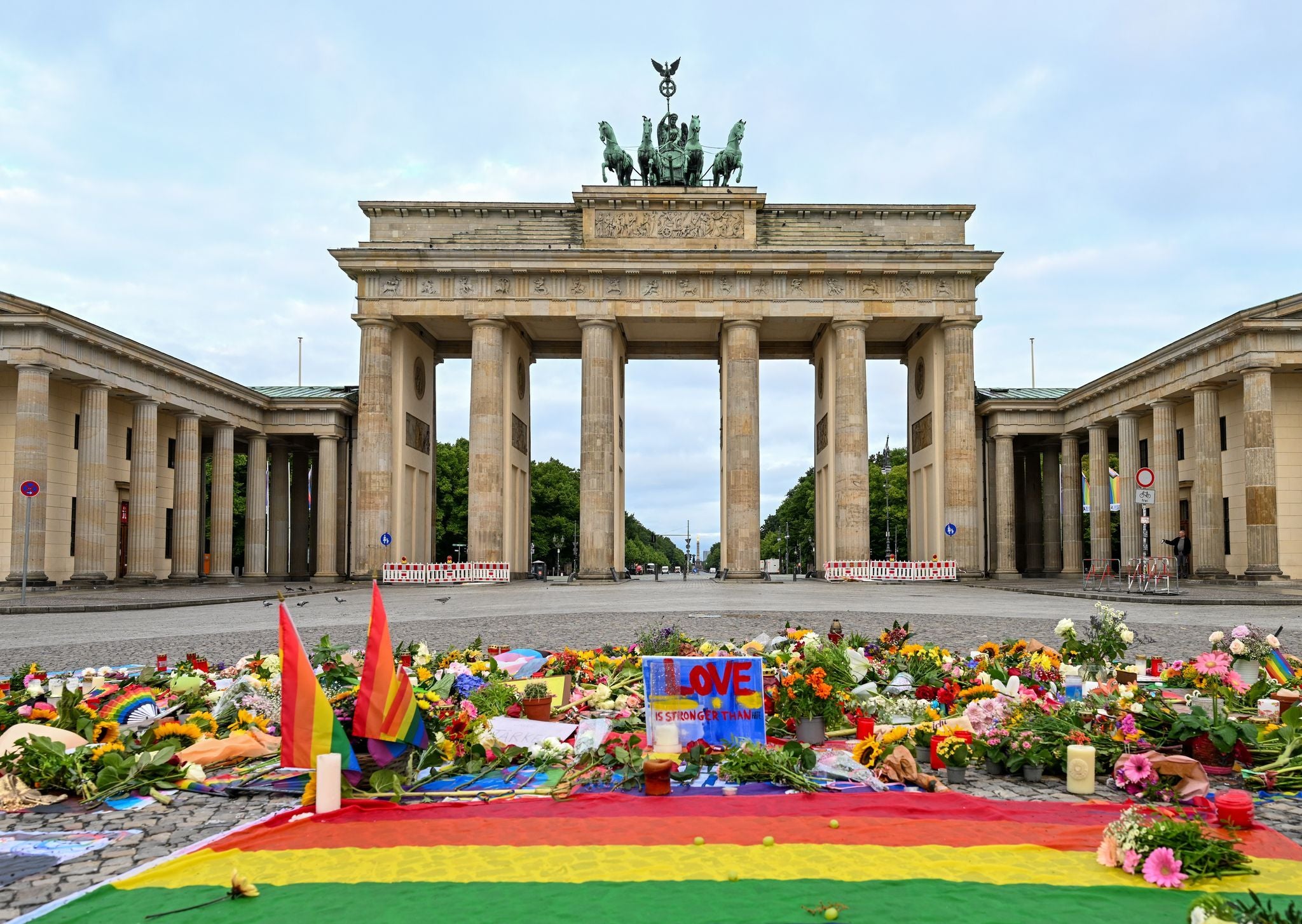 Vor dem Brandenburger Tor liegen Blumen, Kerzen, Botschaften und eine Regenbogenflagge auf dem Boden.