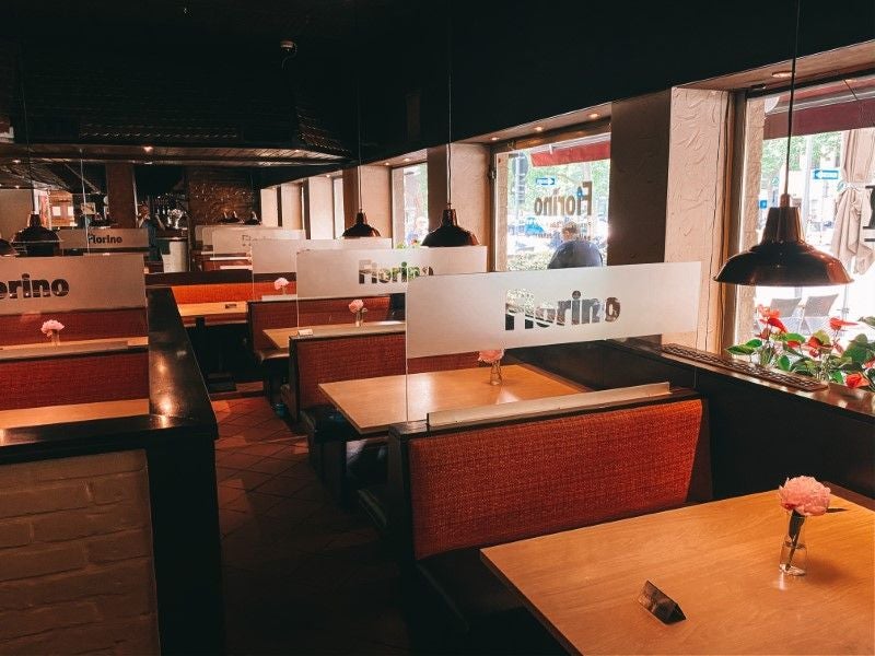 Gemütliches Restaurant mit Holz- und Polsterbänken, Einzelblumen auf Tischen, Fenster zur Straße.