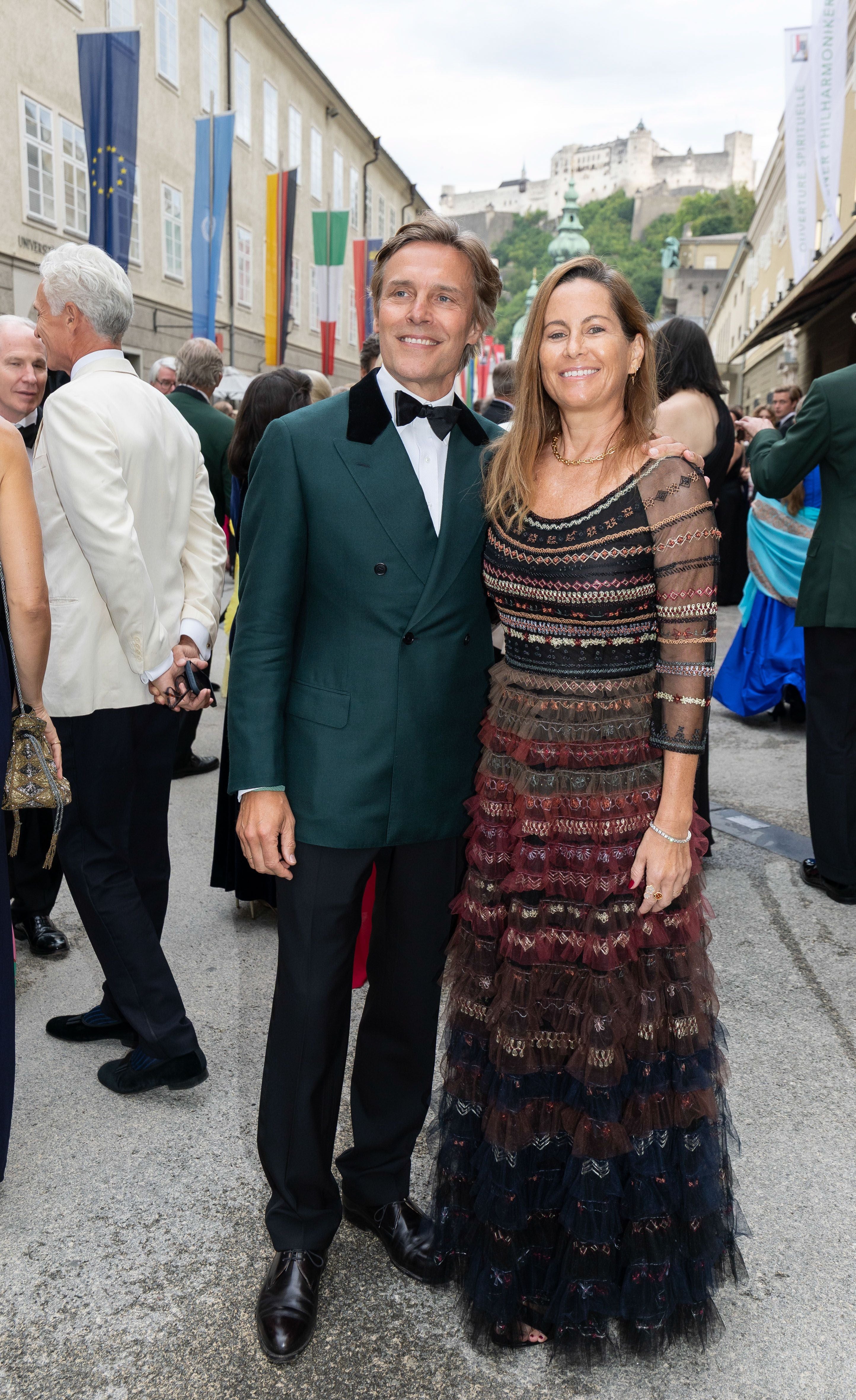 Ein elegant gekleidetes Paar steht lächelnd bei der Salzburger Festspiele Premiere im Freien.
