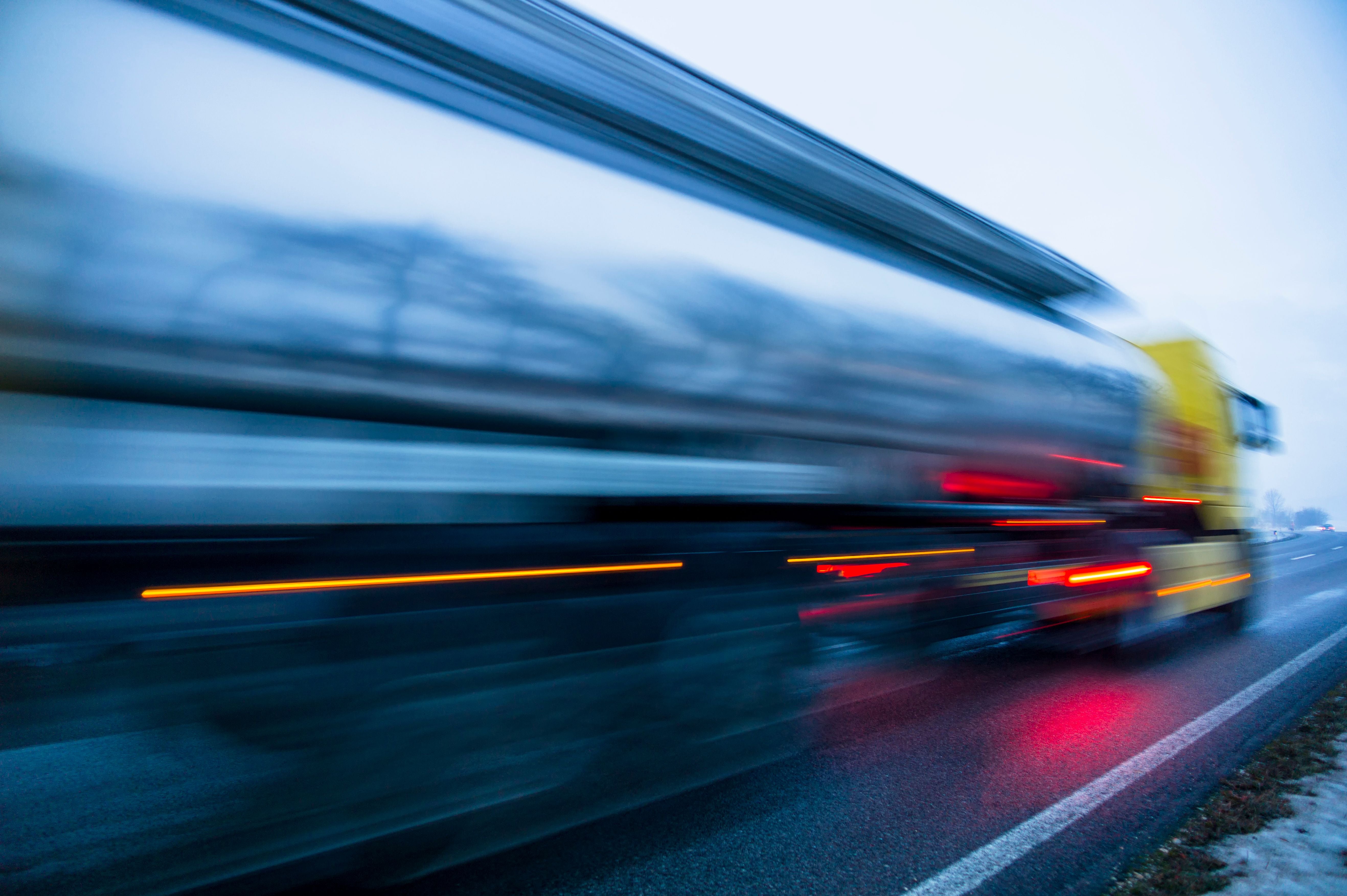 Unscharfer, sich schnell bewegender LKW auf nasser Straße bei Tageslicht.