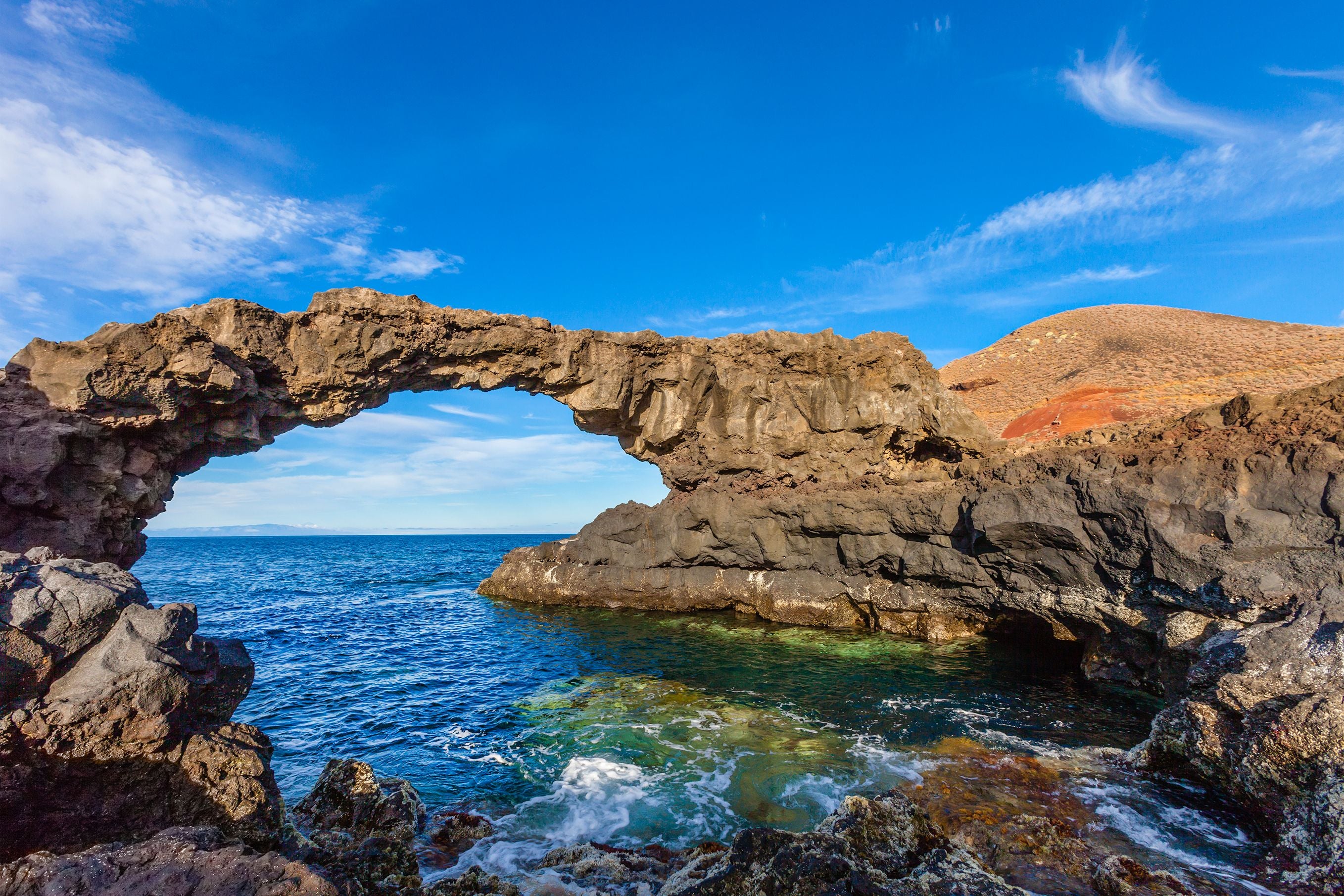 Natürliche Felsbrücke aus Vulkangestein am Meer unter blauem Himmel auf El Hierro, Kanarische Inseln.