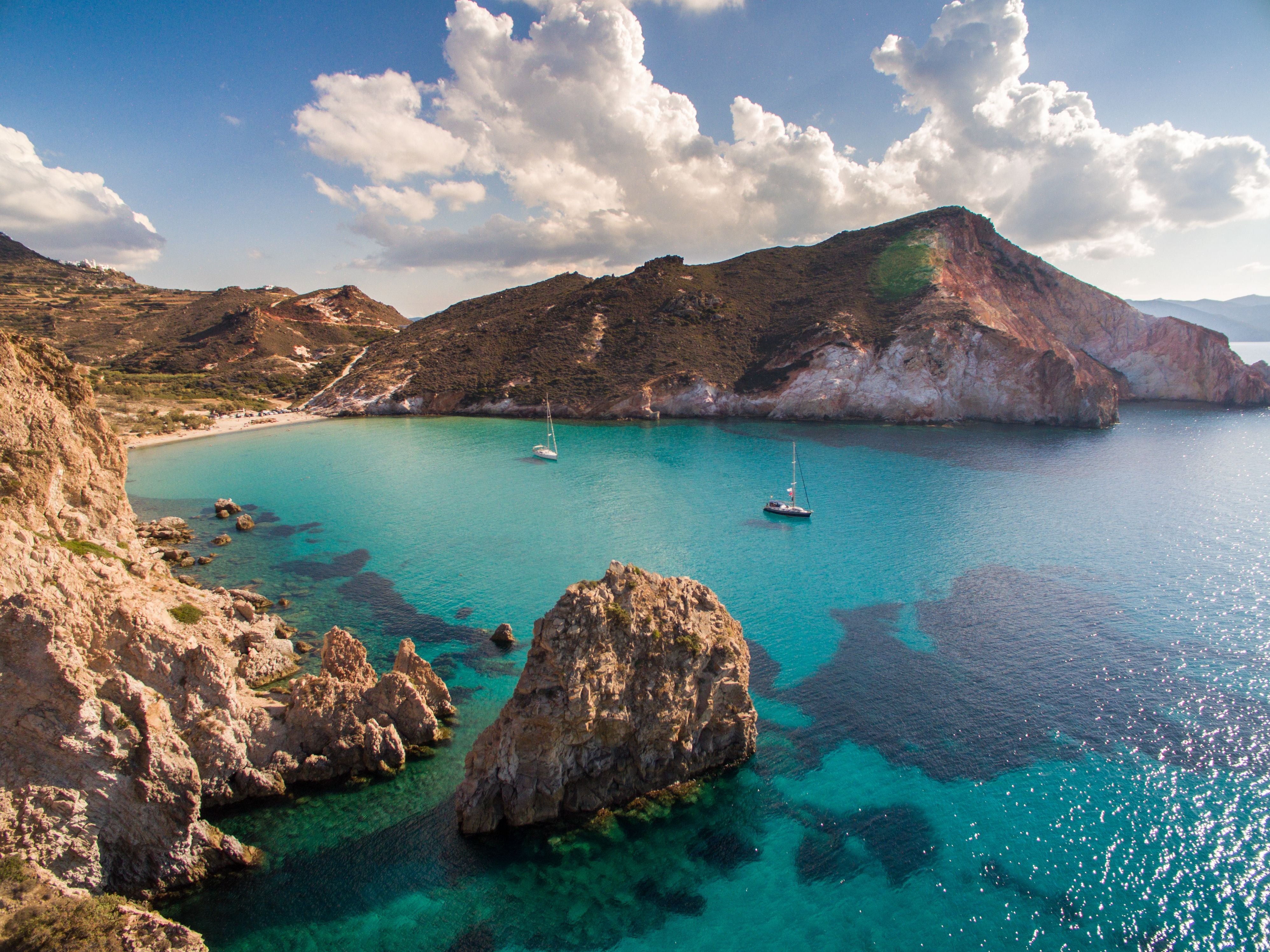 Bucht mit klarem, türkisfarbenem Wasser, zwei Segelbooten und felsigem Ufer auf Milos, Griechenland.
