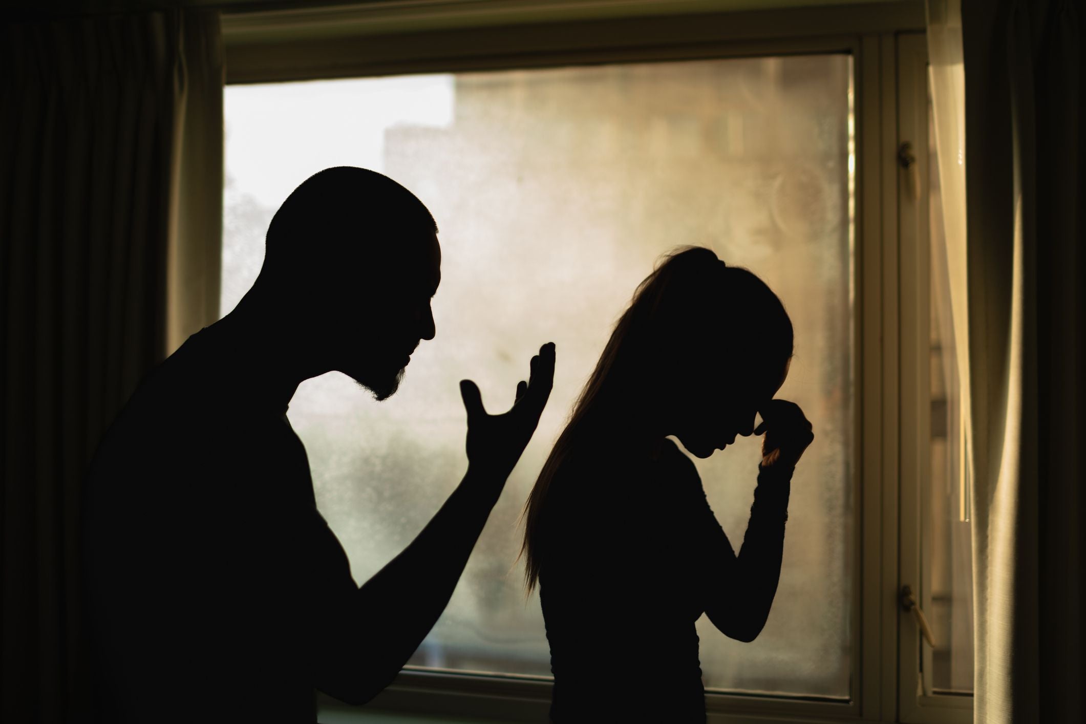 Schatten eines Mannes, der eine Frau anschreit; sie hält den Kopf traurig gesenkt.