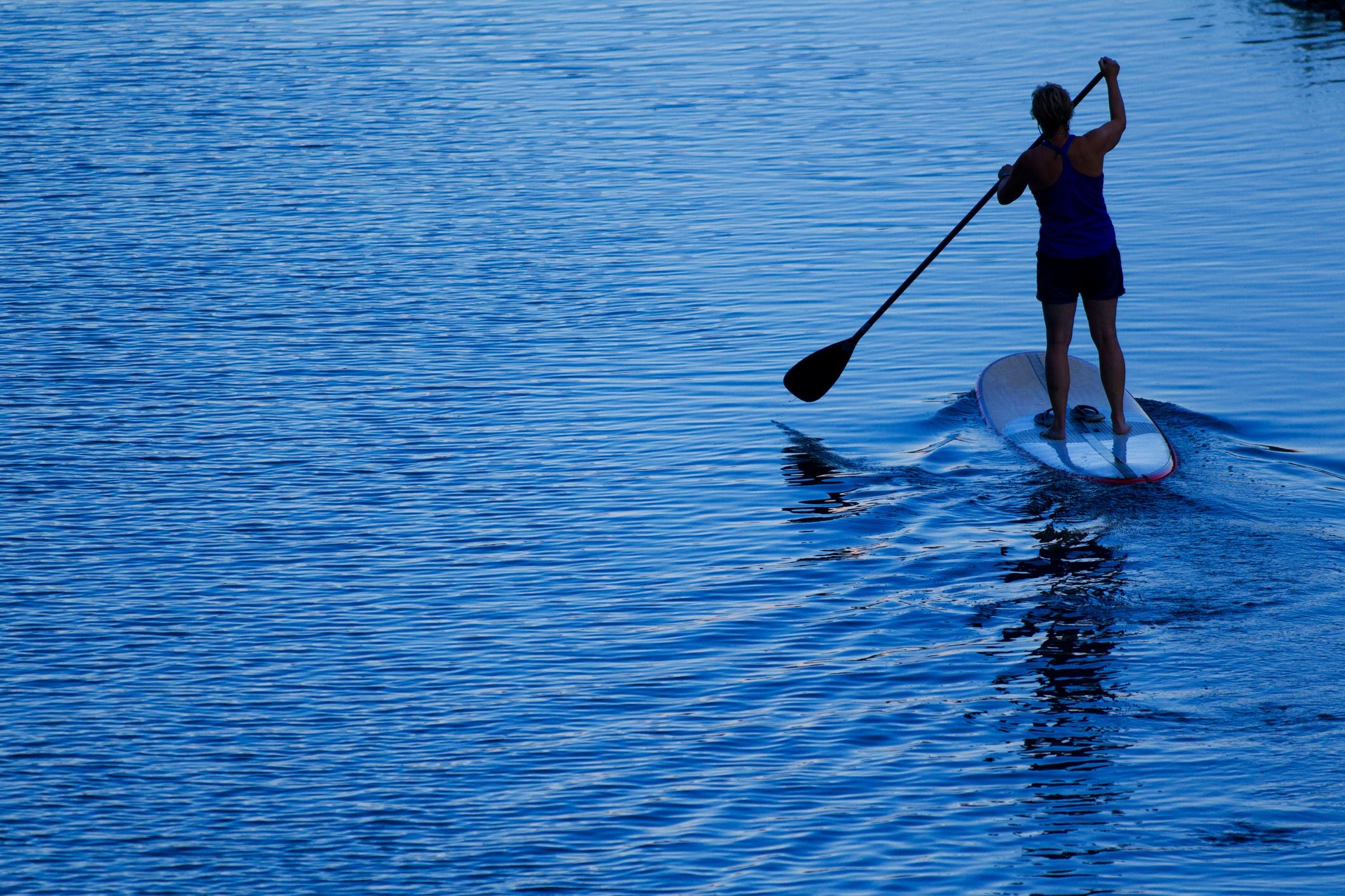 Frau paddelt abends auf einem Stand-Up-Paddleboard über ruhiges Wasser.