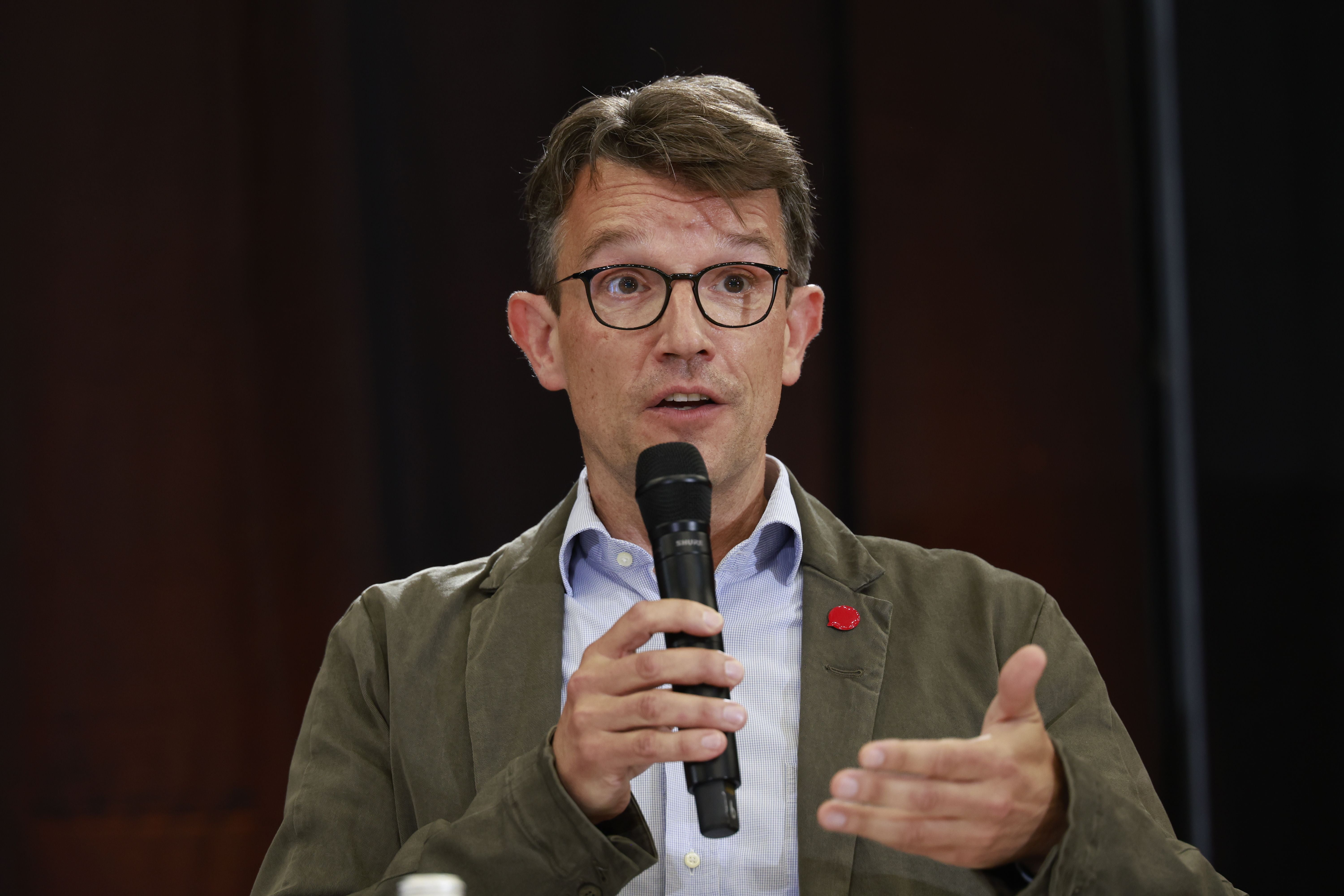 Ein Mann mit Brille spricht in ein Mikrofon und gestikuliert während einer Diskussion.