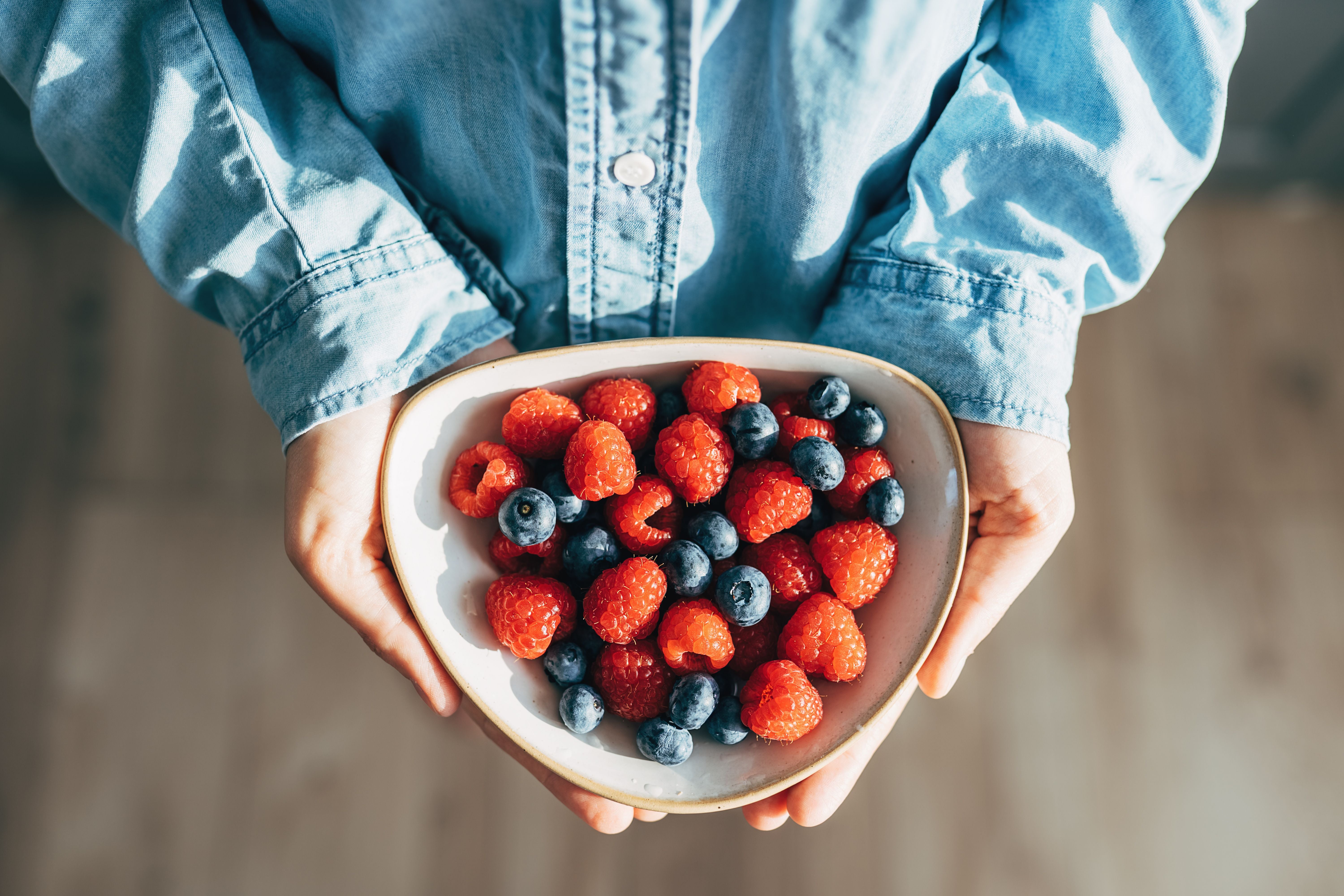 Person hält einen Teller mit Himbeeren und Blaubeeren in den Händen.