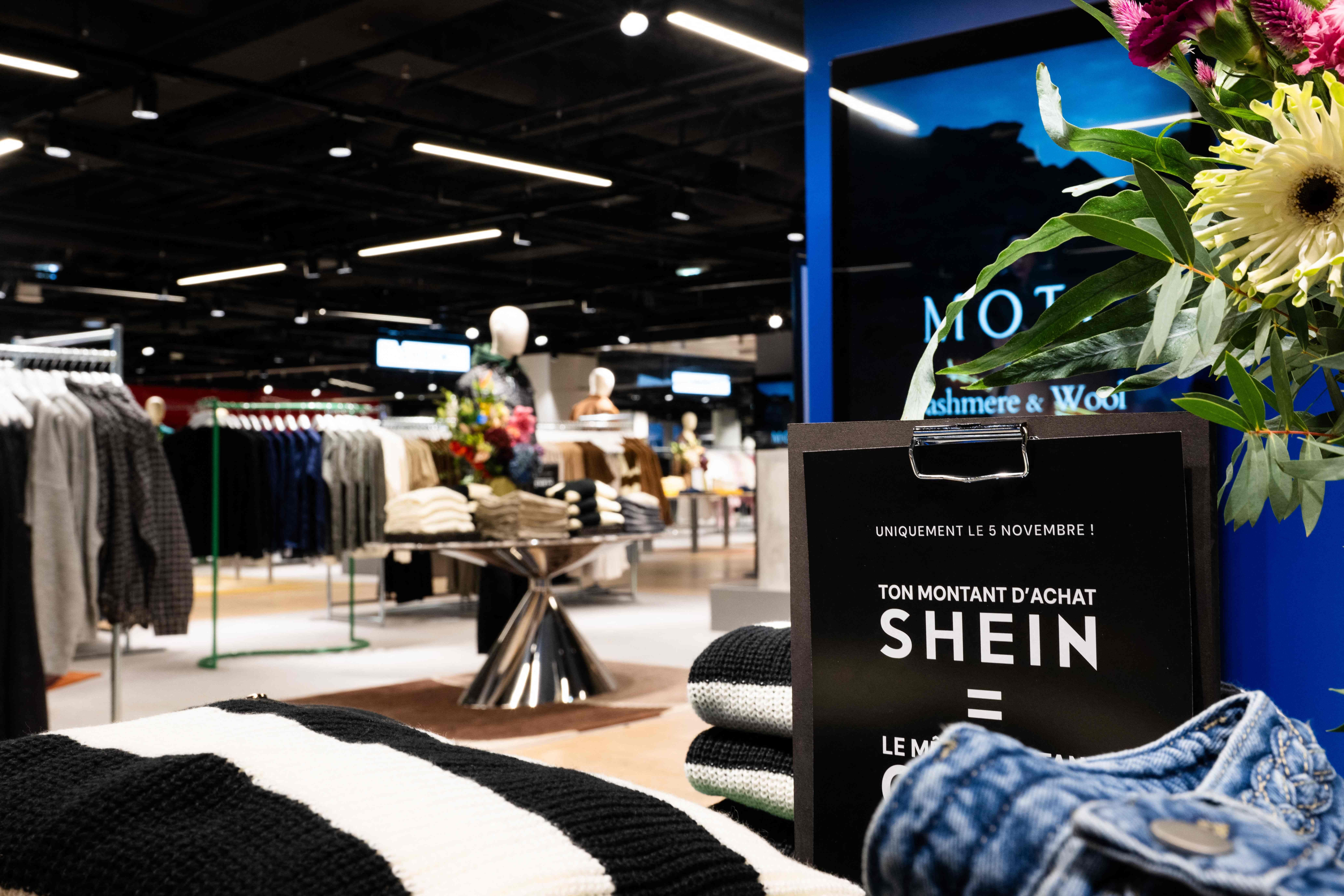 Kleiderständer, Blumen und ein Schild mit dem Shein-Logo in einem Pariser Kaufhaus.