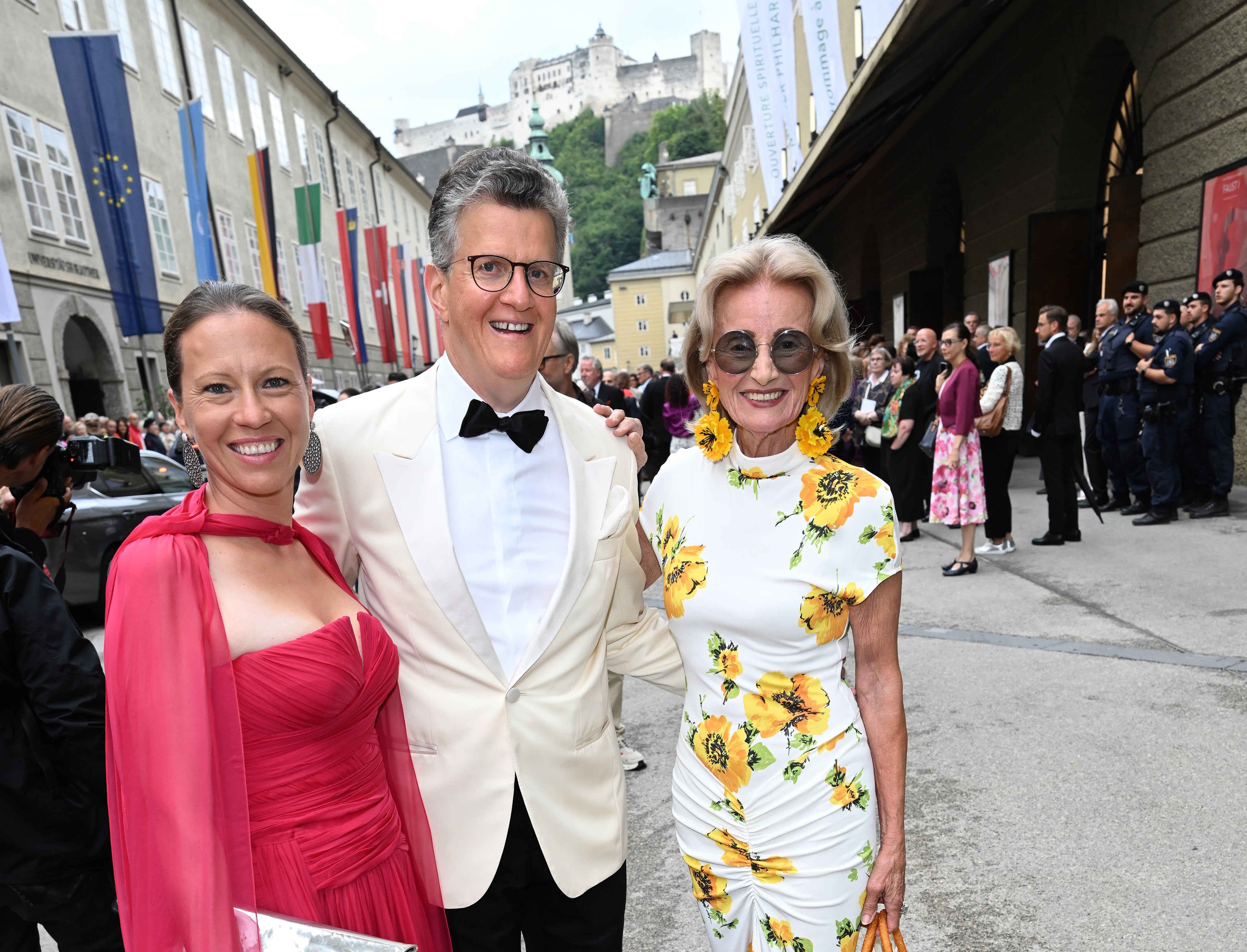 Drei elegant gekleidete Personen posieren lächelnd vor dem Festspielhaus in Salzburg.