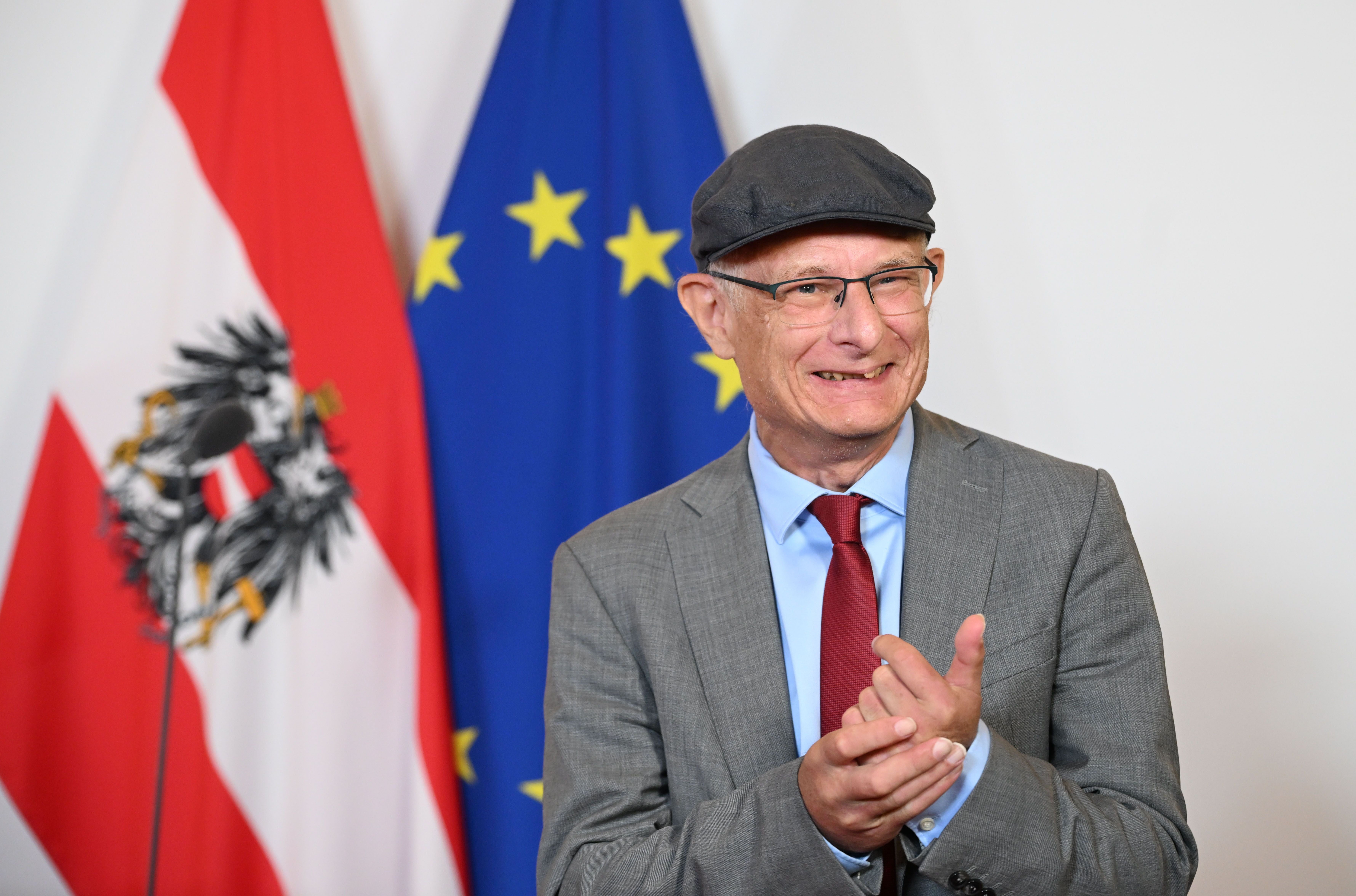 Ein Mann im Anzug und mit Schirmmütze klatscht, im Hintergrund EU- und Österreich-Flagge.