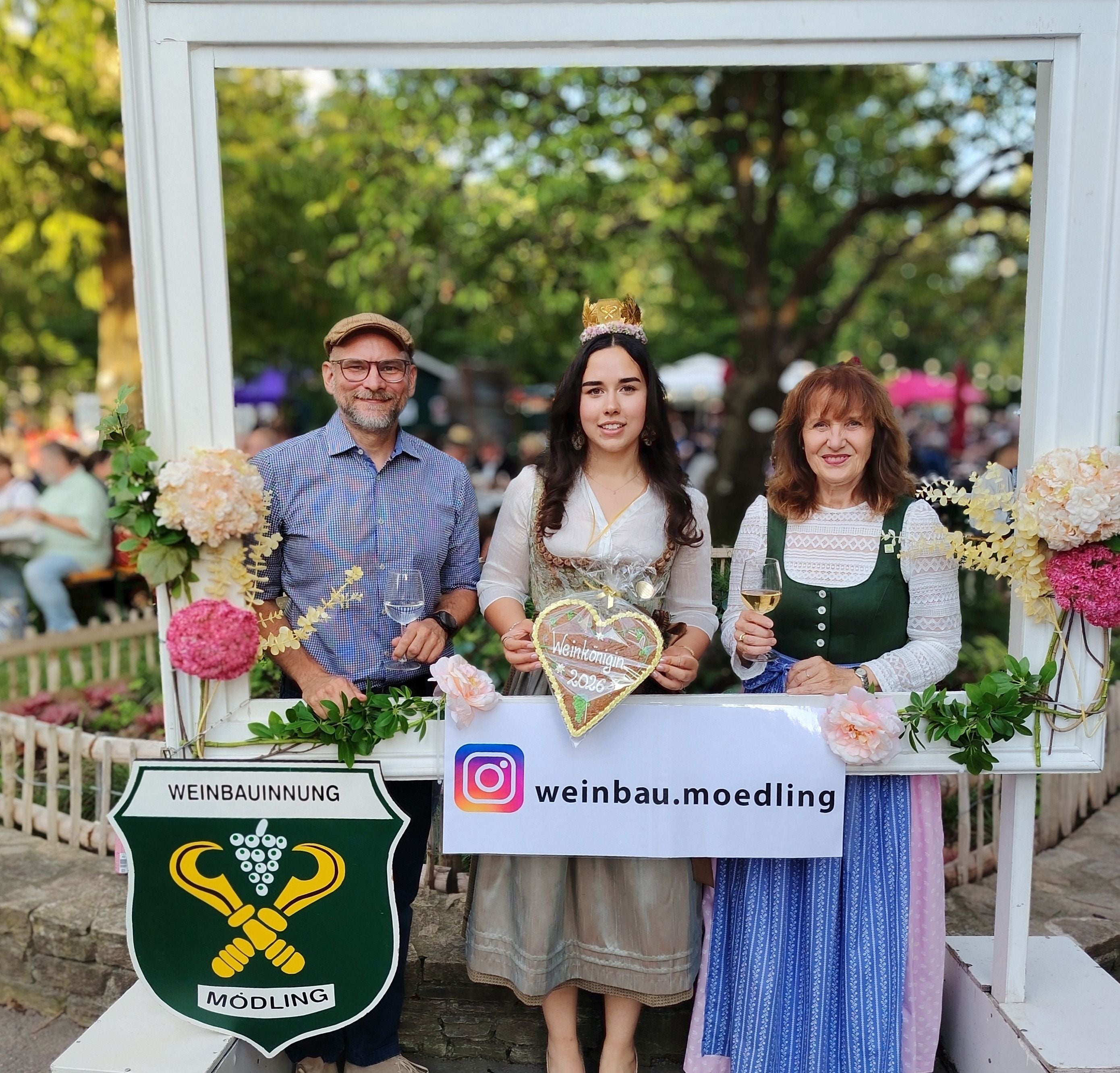 Drei Personen im Trachtenstil posieren mit Weingläsern bei einem Weinfest in Mödling.