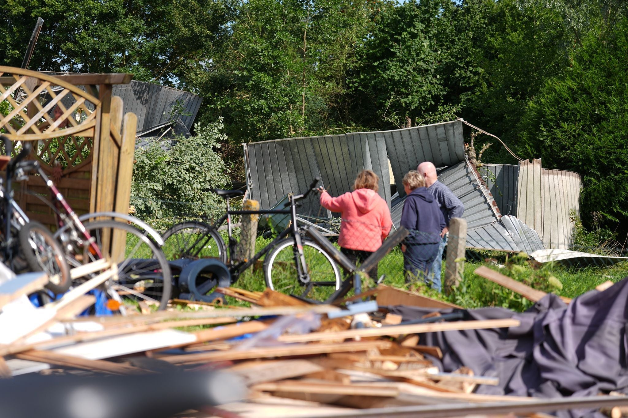 Drei Menschen betrachten zerstörte Garagen und Trümmer nach einem Unwetter im Garten.