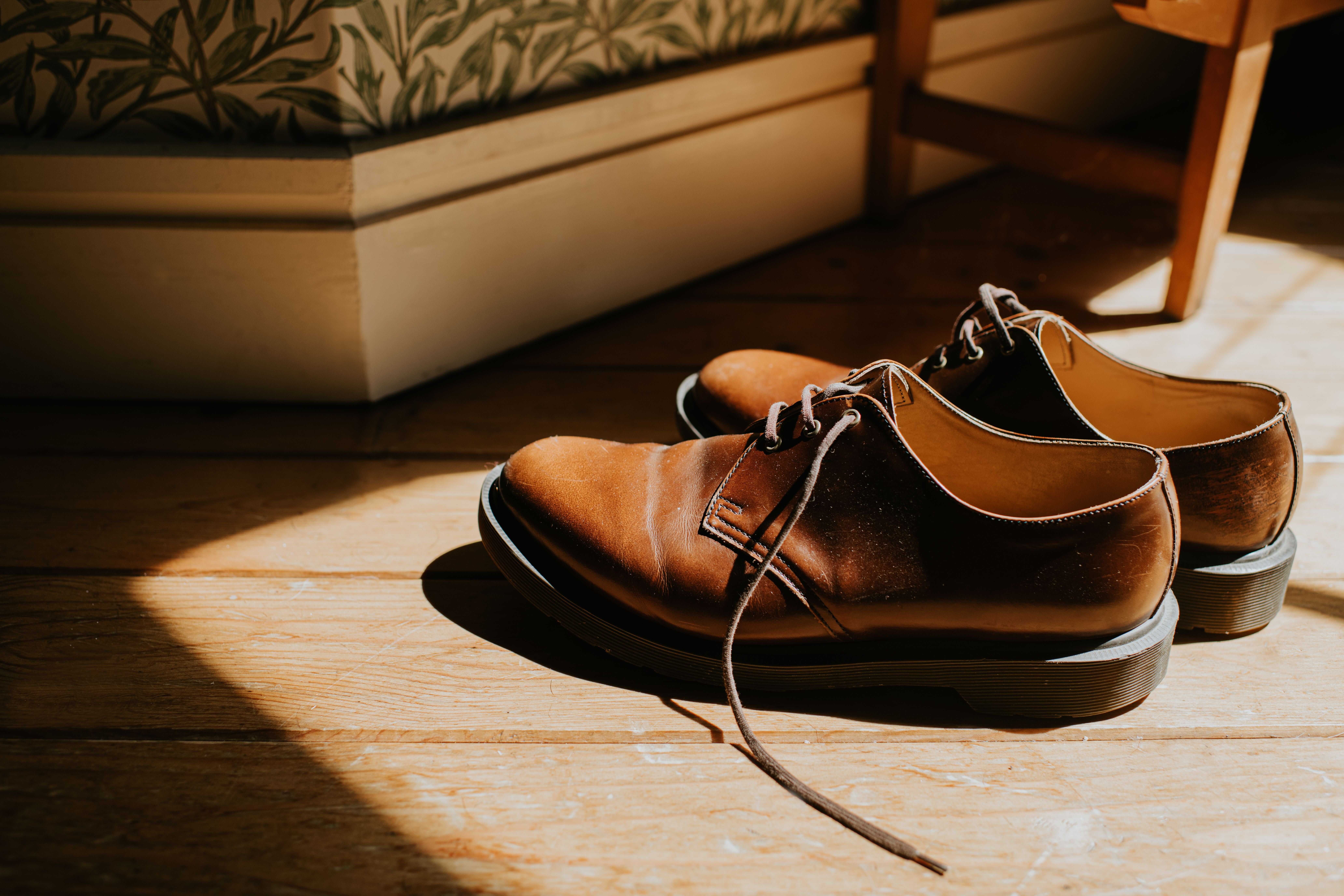 Ein Paar braune Lederschuhe steht in Sonnenlicht auf einem hölzernen Fußboden.