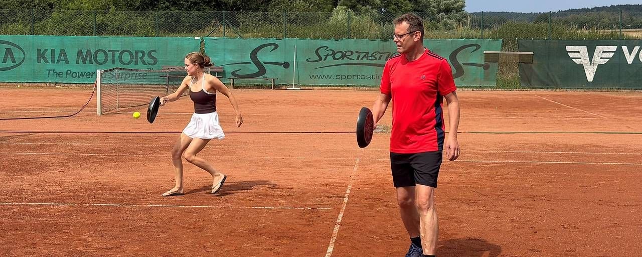 Ein Mann und eine Frau spielen gemeinsam ein Spiel mit Schlägern und Ball auf einem Sandplatz.