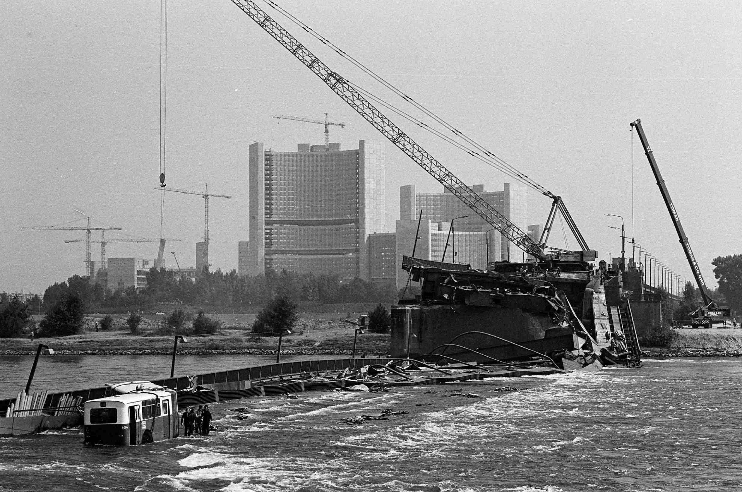Schwarzweißfoto vom Einsturz der Wiener Reichsbrücke 1976 mit Kränen und Bus im Wasser.