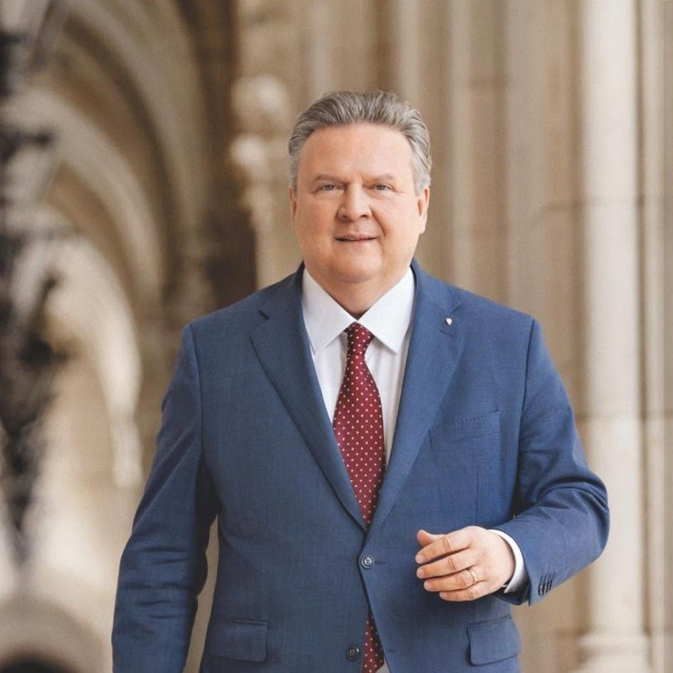 Ein Mann im blauen Anzug mit roter Krawatte steht in einem historischen Gebäude.
