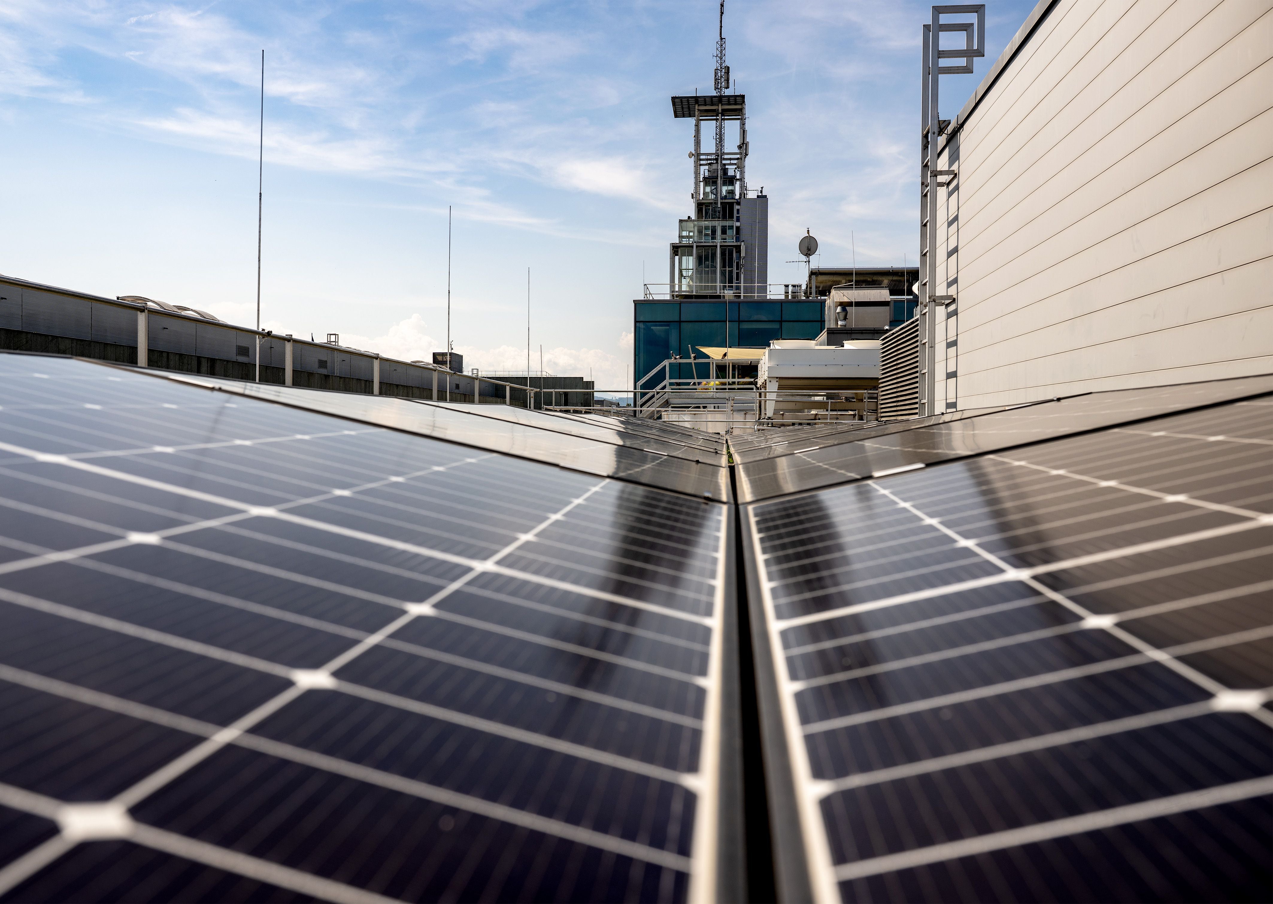 Solarmodule auf einem Flachdach mit Gebäudetechnik im Hintergrund bei sonnigem Wetter.
