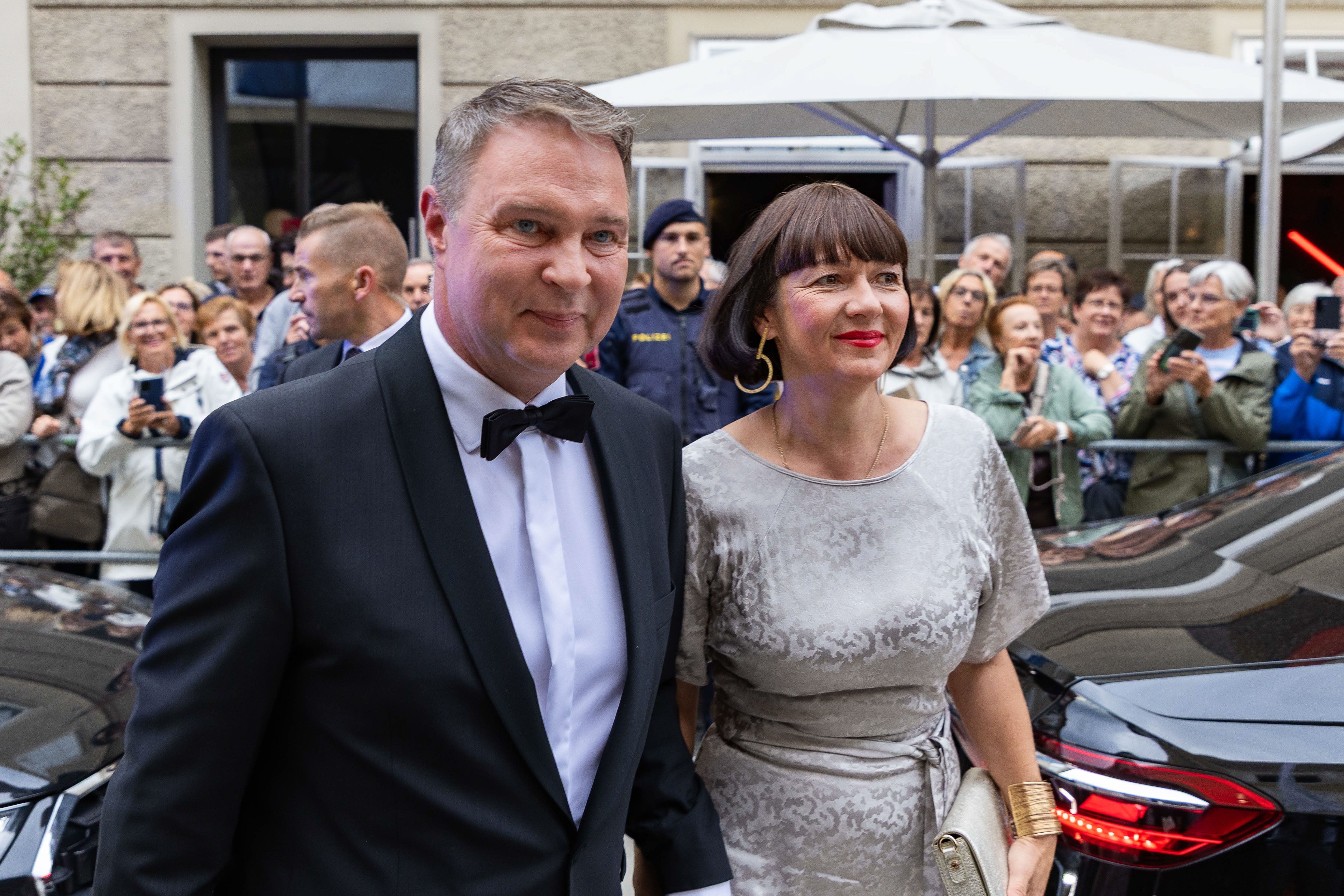 Ein Mann im Smoking und eine Frau im Kleid posieren vor einer Menschenmenge bei einer Premiere.