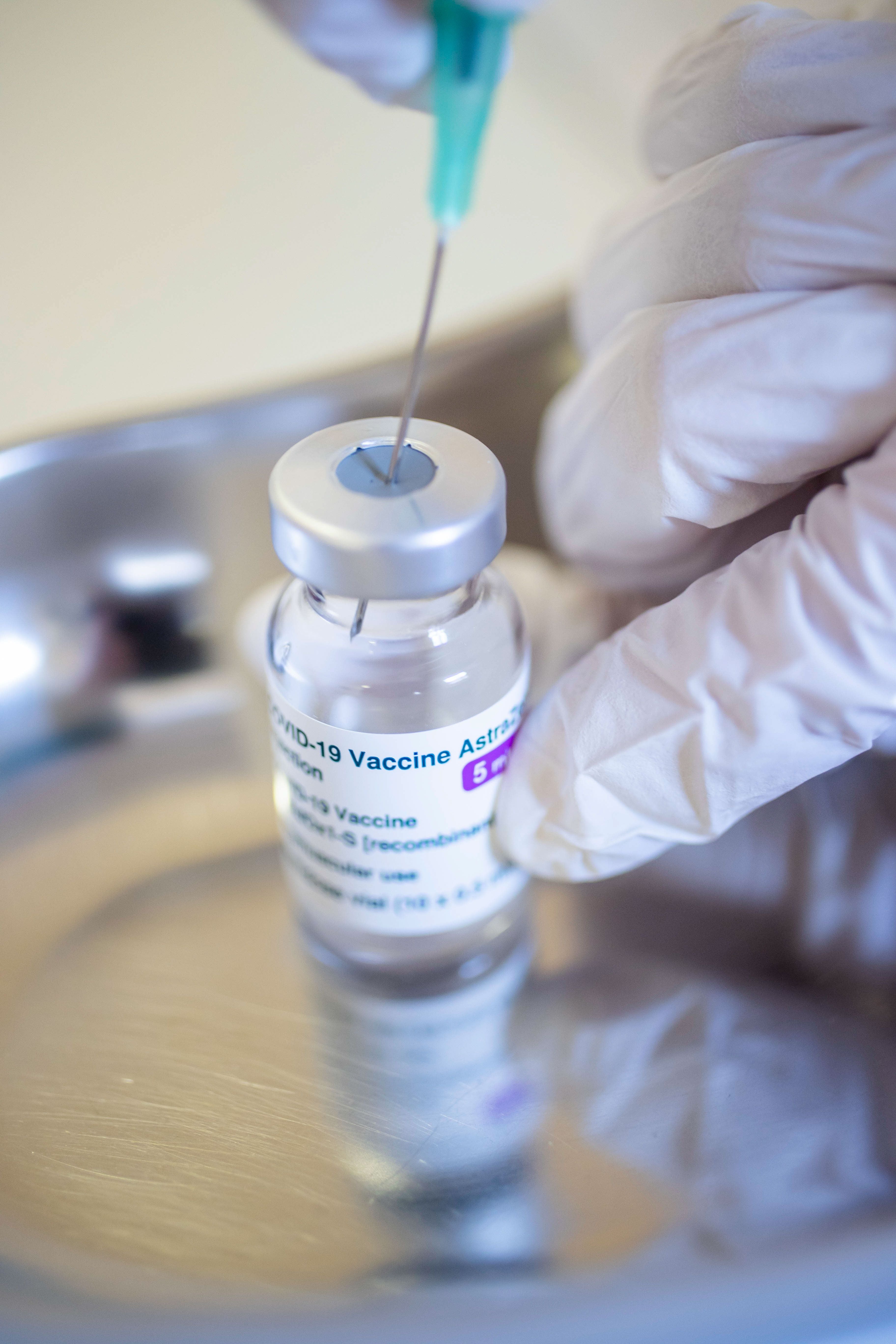 Hand mit Handschuh zieht COVID-19-AstraZeneca-Impfstoff mit einer Spritze auf.
