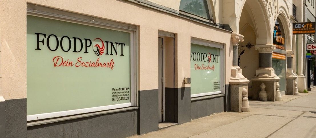 Schaufenster eines Sozialmarkts namens Foodpoint in Wien mit Werbetext auf der Scheibe.