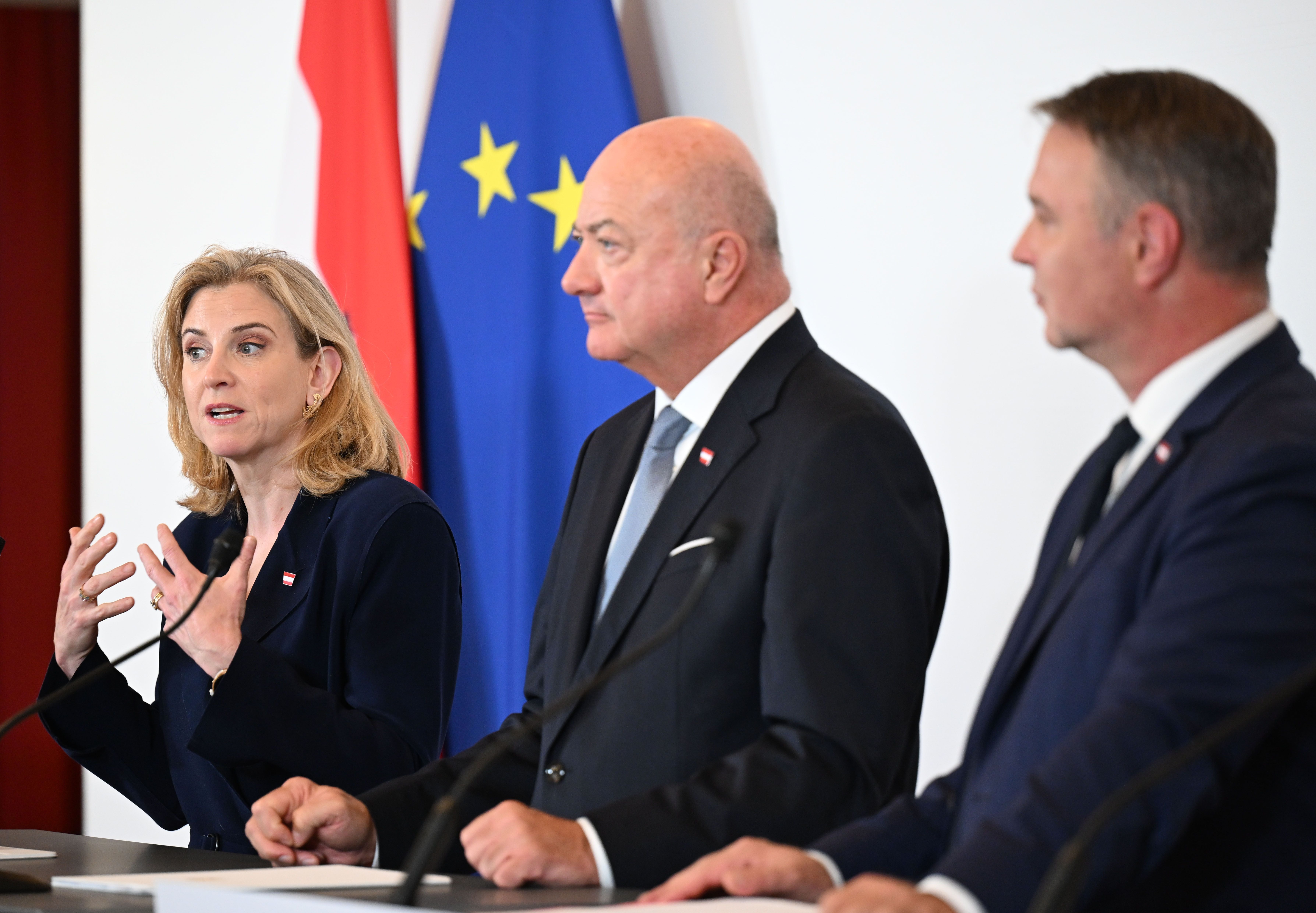 Drei Politiker sprechen bei einer Pressekonferenz vor österreichischer und EU-Flagge.