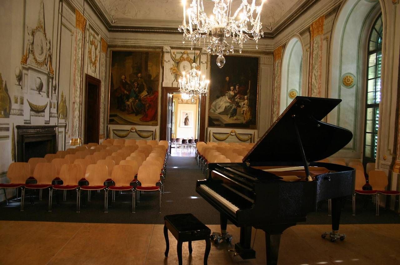Konzertsaal mit Flügel, Stuhlreihen, Kronleuchtern und Wandgemälden im Schloss Kirchstetten.