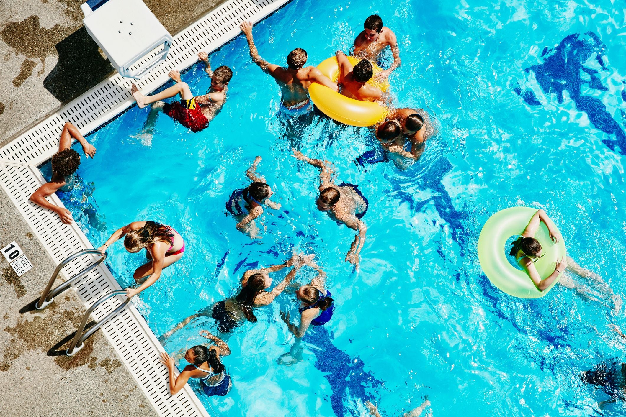 Mehrere Jugendliche spielen und schwimmen gemeinsam in einem Außenpool, Ansicht von oben.