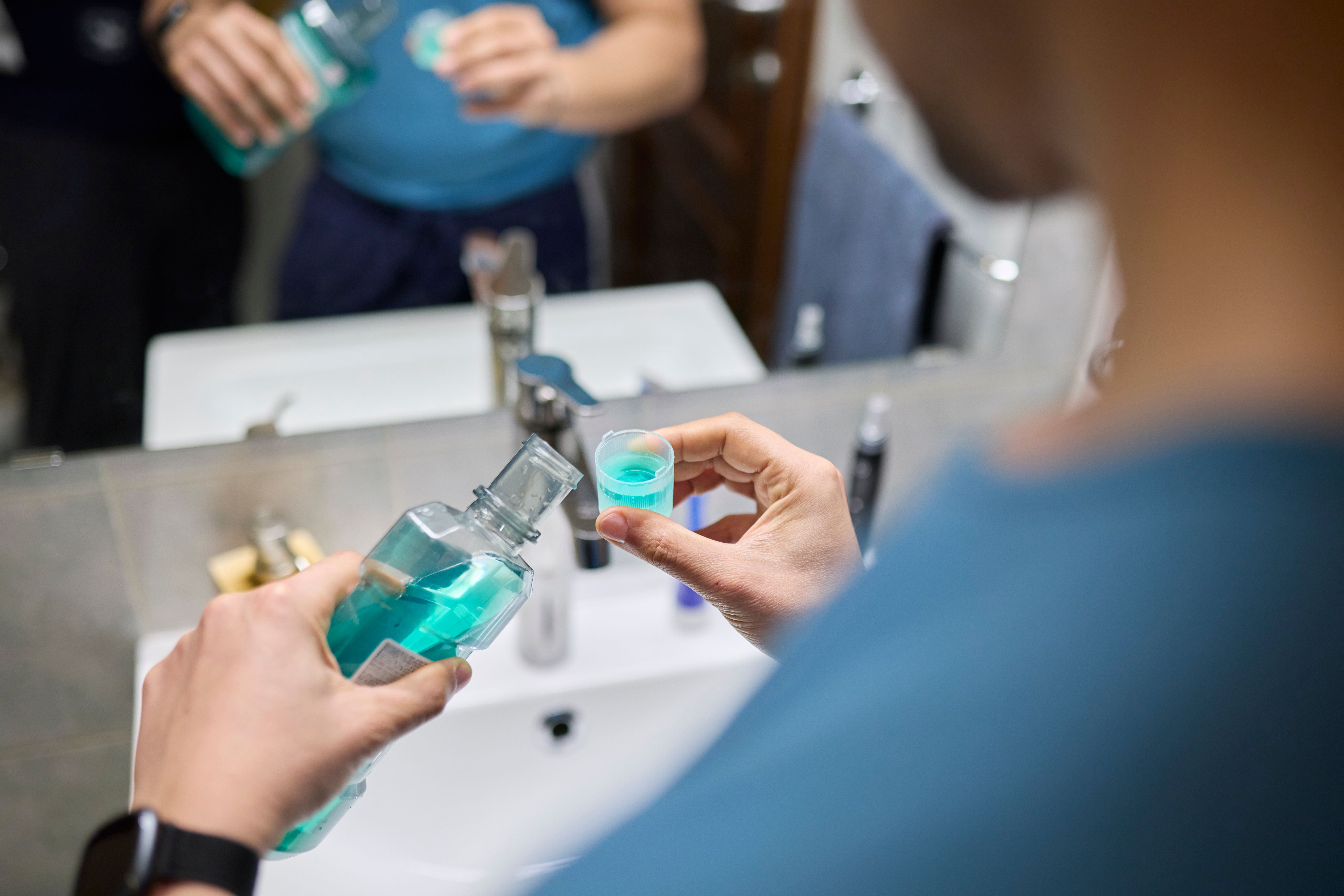 Ein Mann gießt Mundspülung in einen Dosierbecher am Waschbecken im Badezimmer.