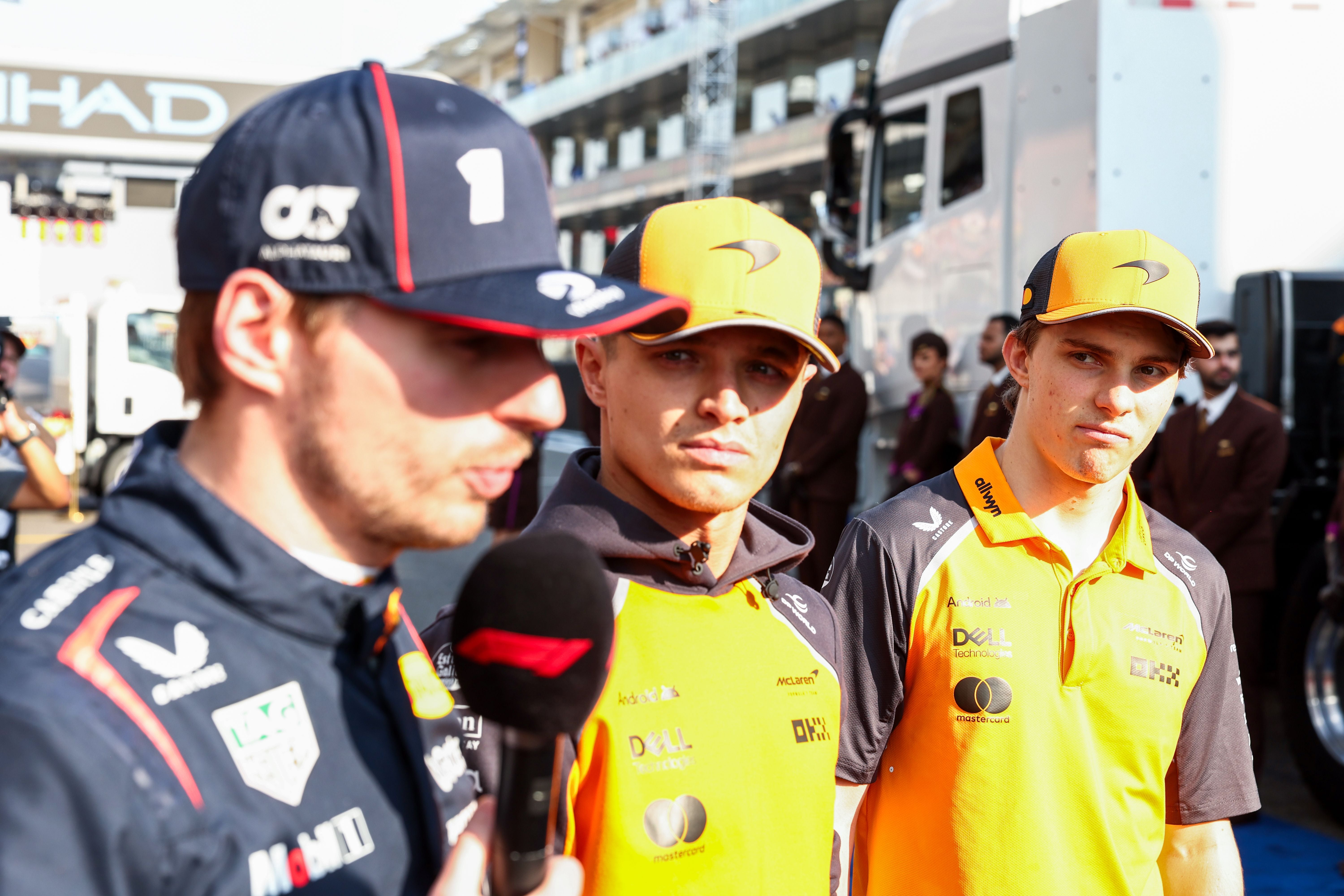 ABU DHABI, UNITED ARAB EMIRATES - DECEMBER 07: Lando Norris of McLaren and Great Britain and Oscar Piastri of McLaren and Australia listen intently to Max Verstappen of Oracle Red Bull Racing and The Netherlands being interviewed by the media before the drivers parade during the F1 Grand Prix of Abu Dhabi at Yas Marina Circuit on December 07, 2025 in Abu Dhabi, United Arab Emirates. (Photo by Peter Fox/Getty Images)