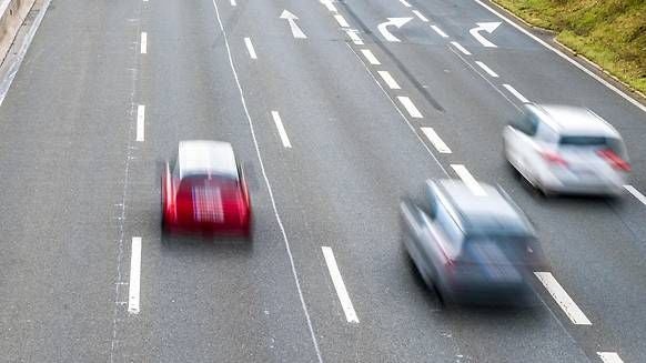 Drei Autos fahren schnell auf einer mehrspurigen Straße mit Fahrbahnmarkierungen.