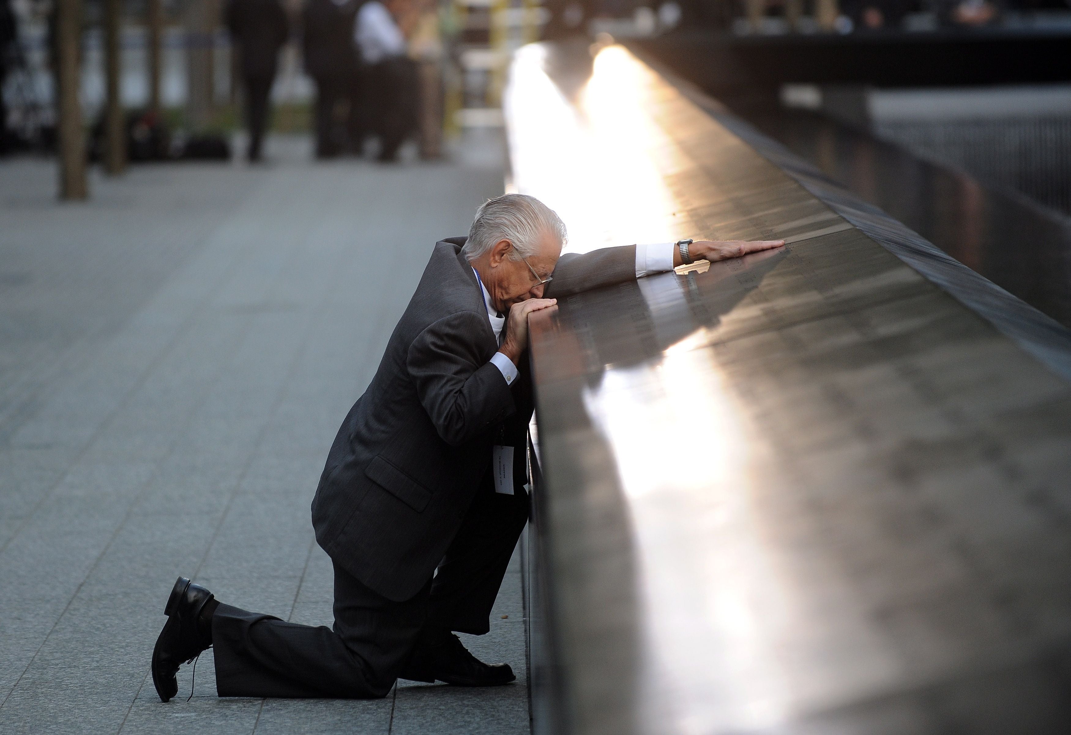 Ein älterer Mann kniet nachdenklich am 9/11-Memorial und berührt einen Namen auf dem Denkmal.