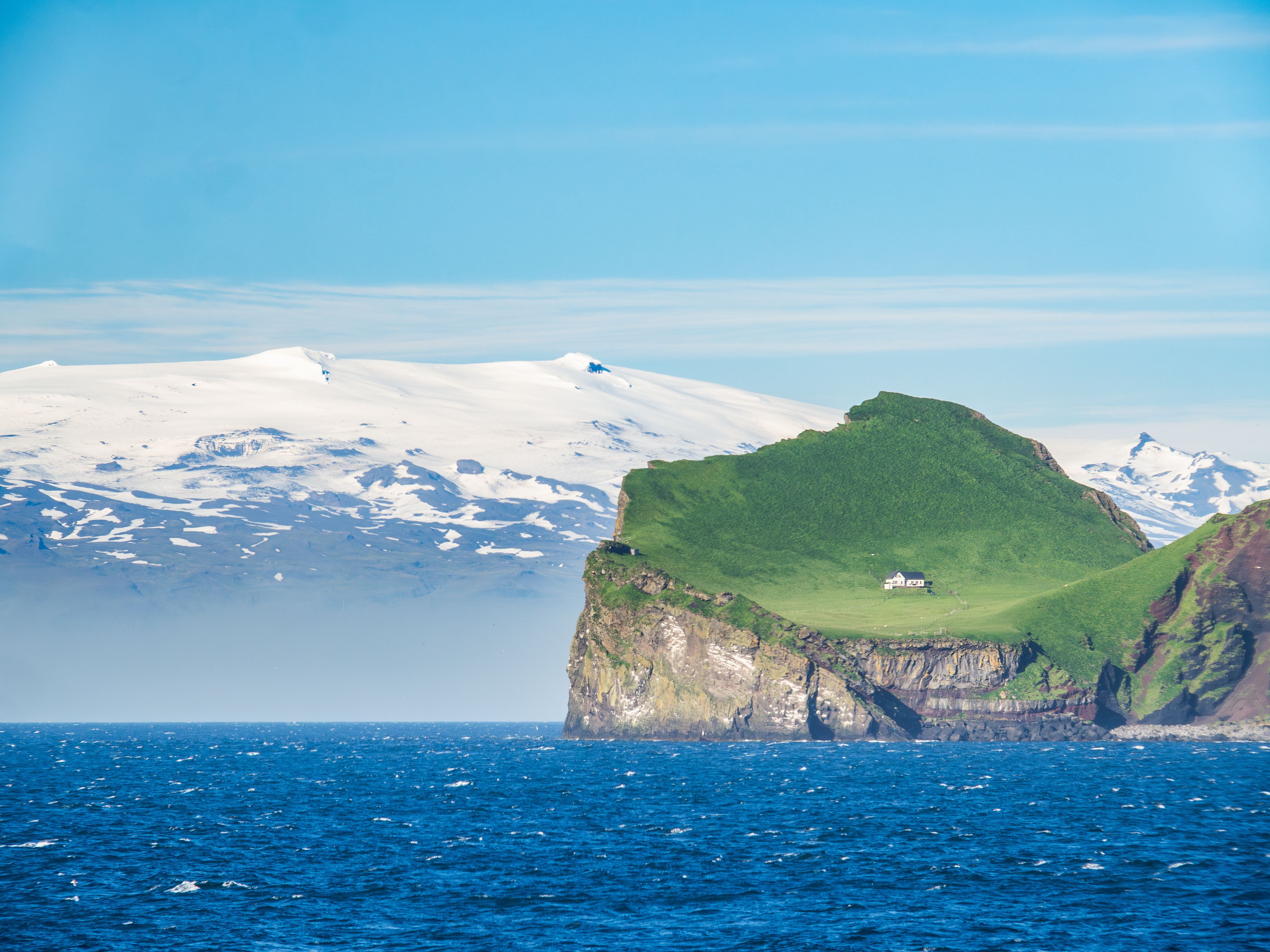 Blick auf die Insel Elliðaey mit einsamem Jagdhaus, dahinter der verschneite Gletscher Eyjafjallajökull.