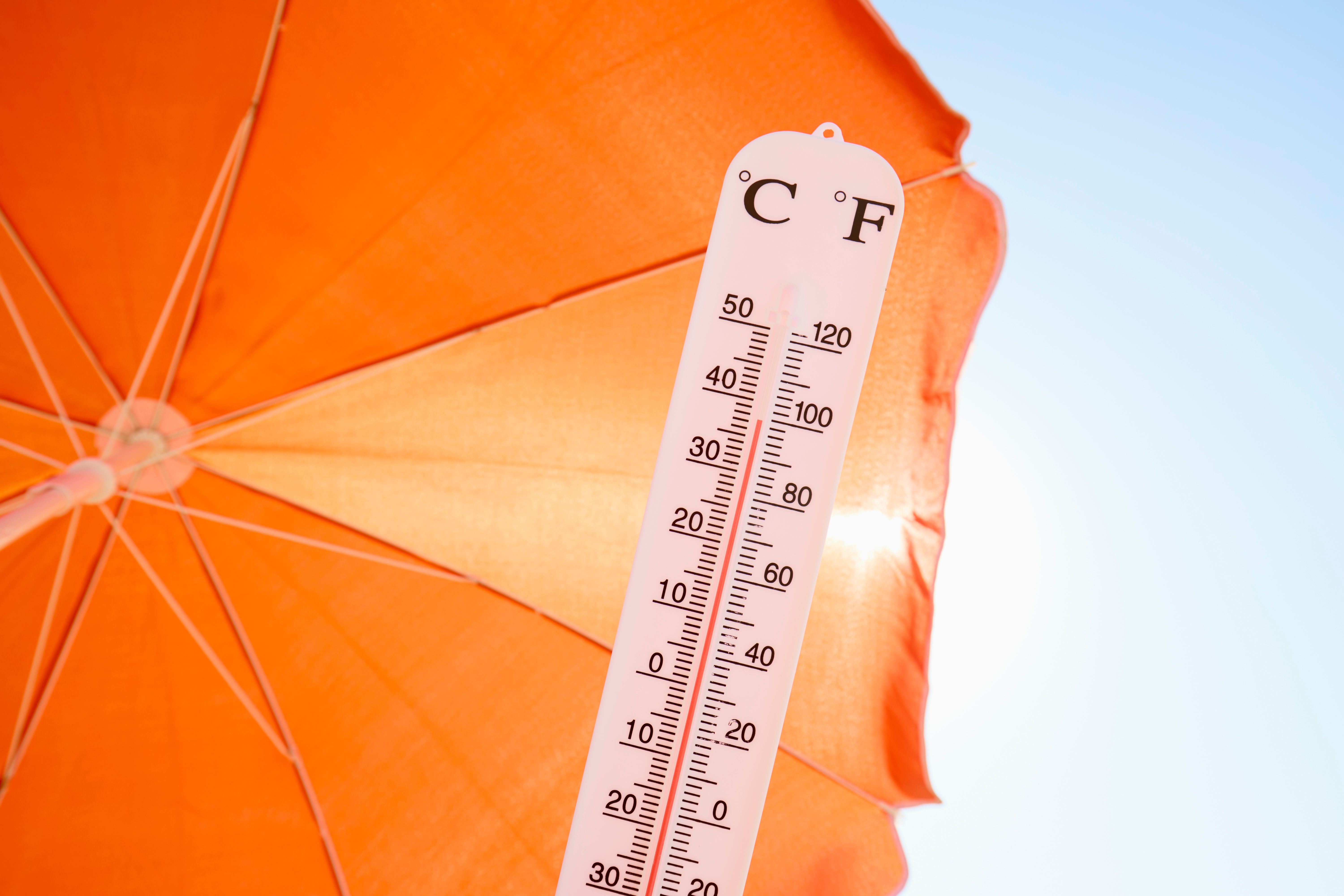 Thermometer zeigt hohe Temperatur vor einem orangefarbenen Sonnenschirm bei klarem Himmel.