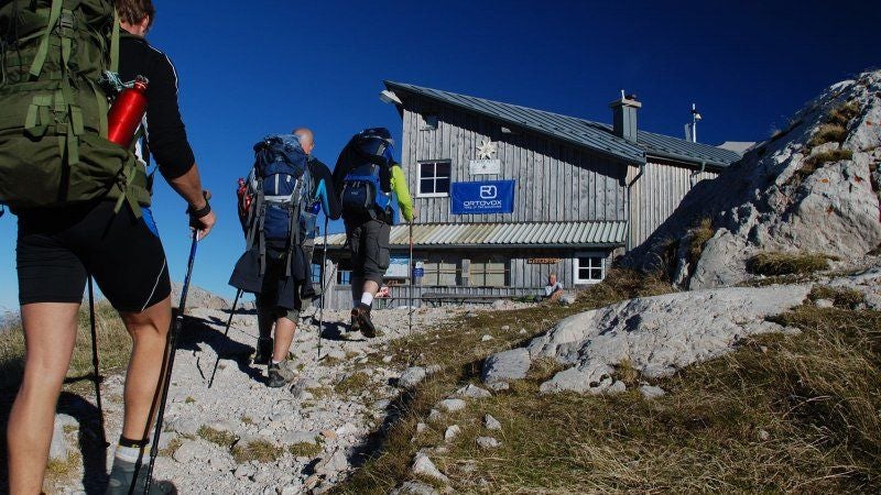 Mehrere Wanderer mit Rucksäcken steigen zu einer Berghütte am Krippenstein auf.