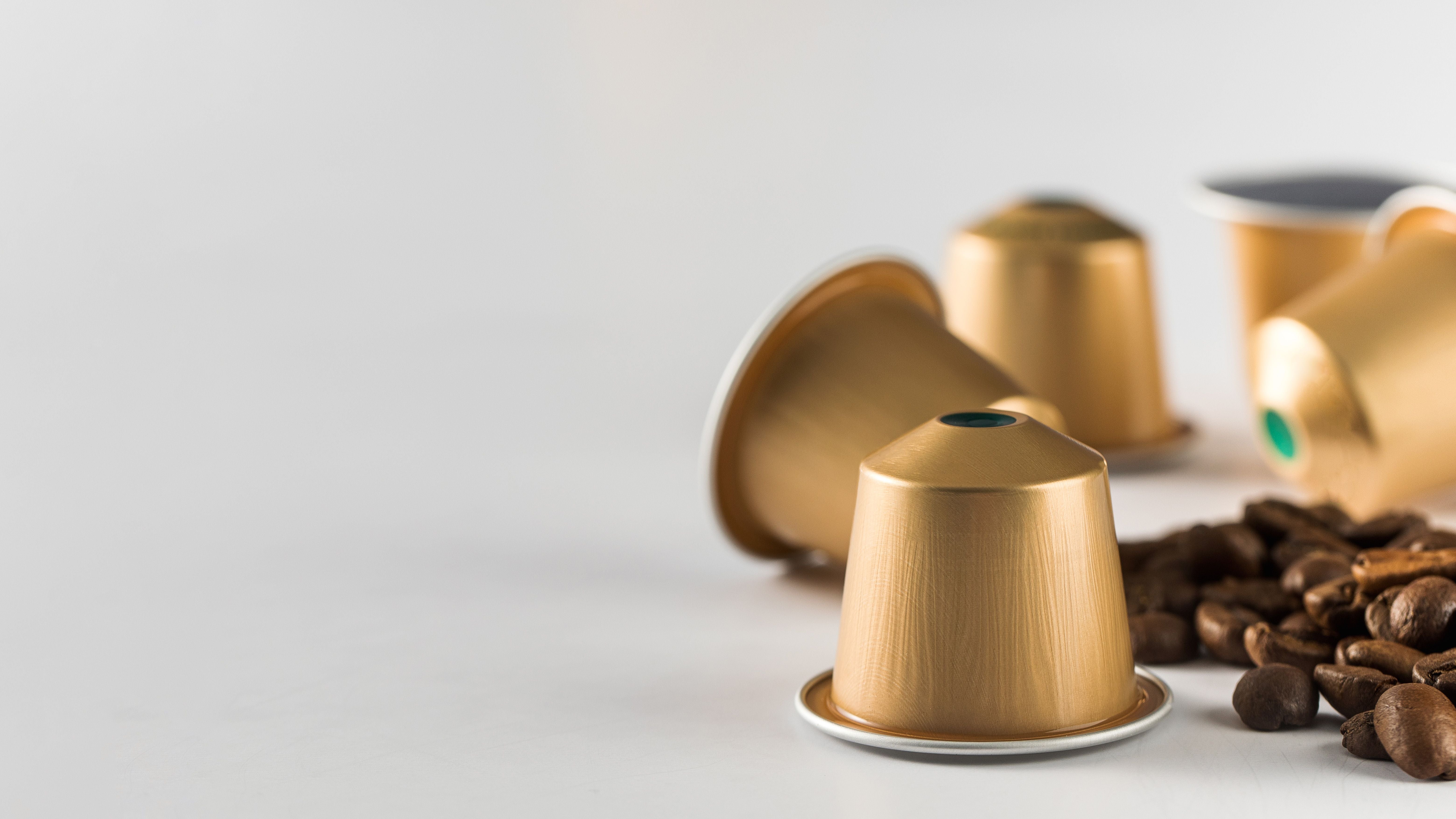 Goldene Kaffeekapseln und Kaffeebohnen auf weißem Hintergrund mit viel Freiraum.