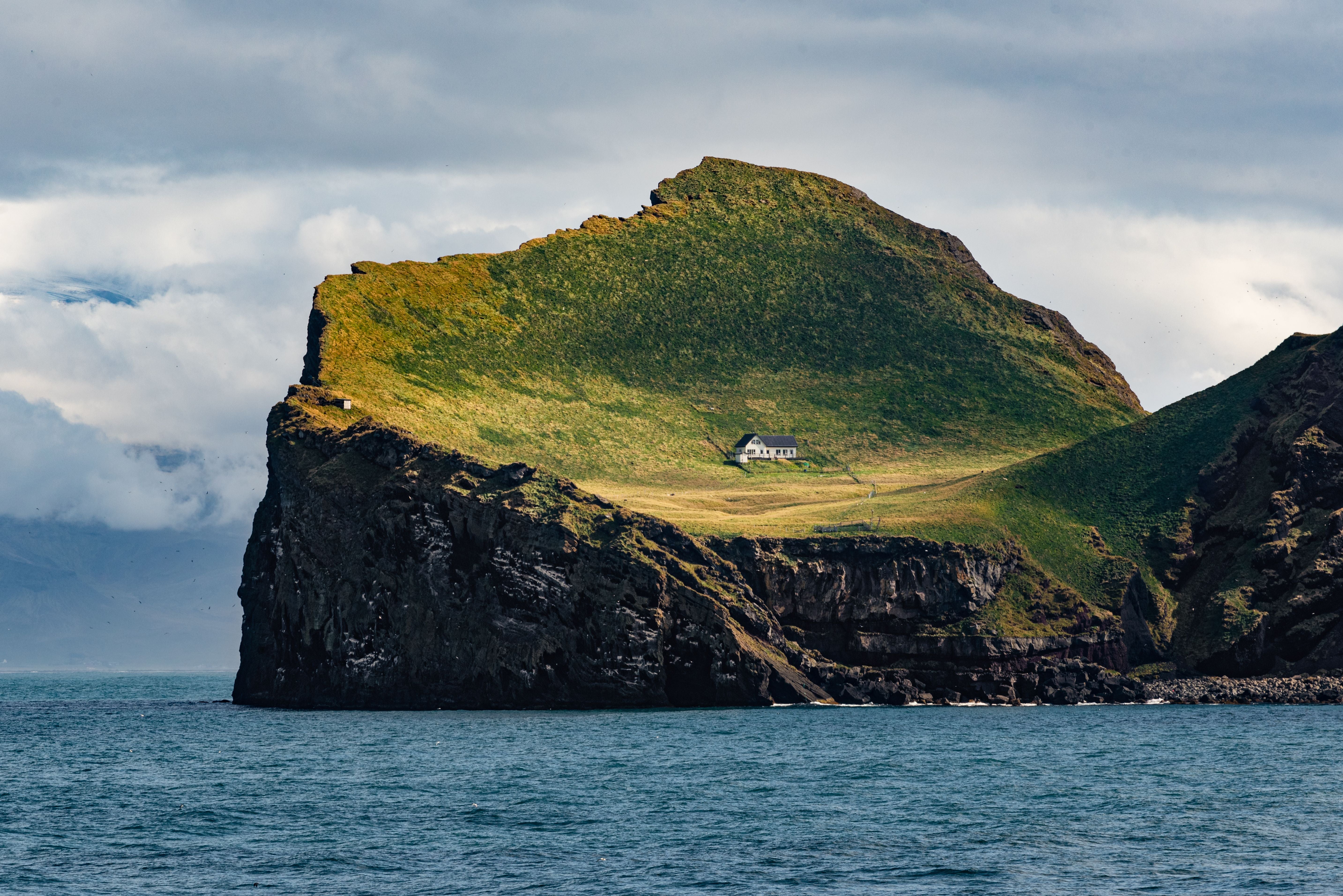 Grüne Insel mit steilen Klippen und einem einzelnen weißen Haus, umgeben vom Meer.