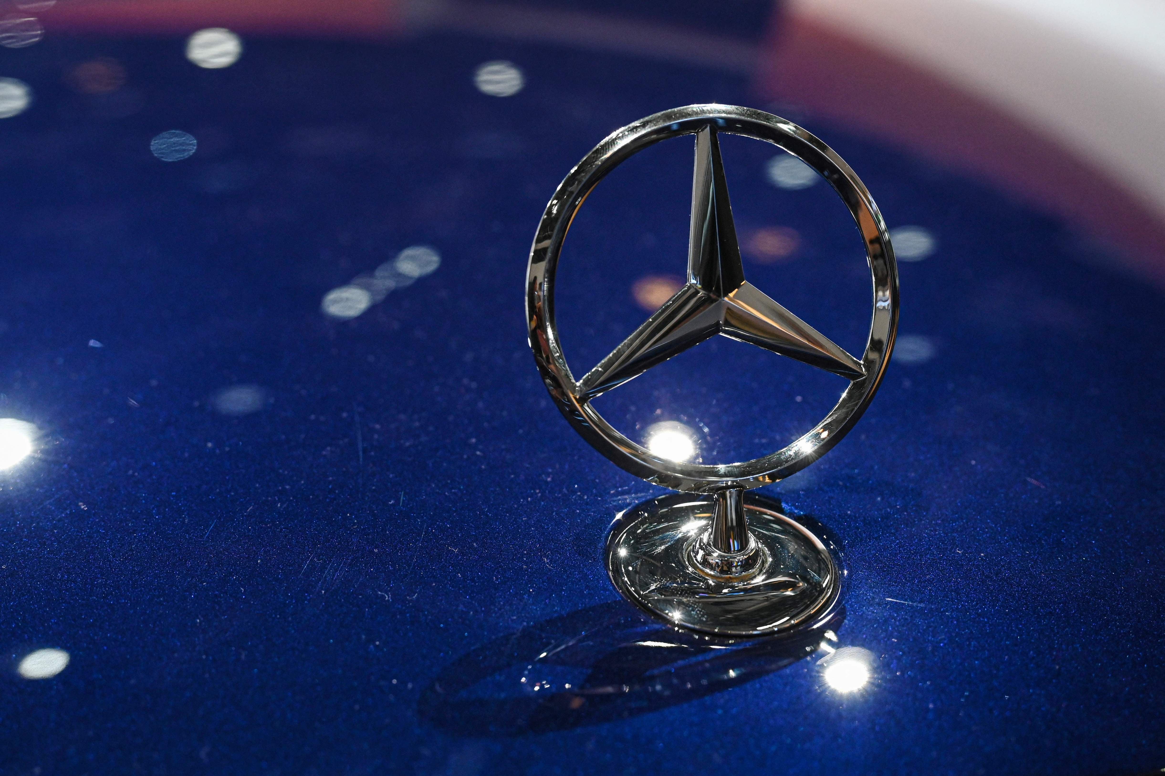 Mercedes-Benz Sternemblem auf blauem Autolack, Nahaufnahme mit Lichtreflexen.