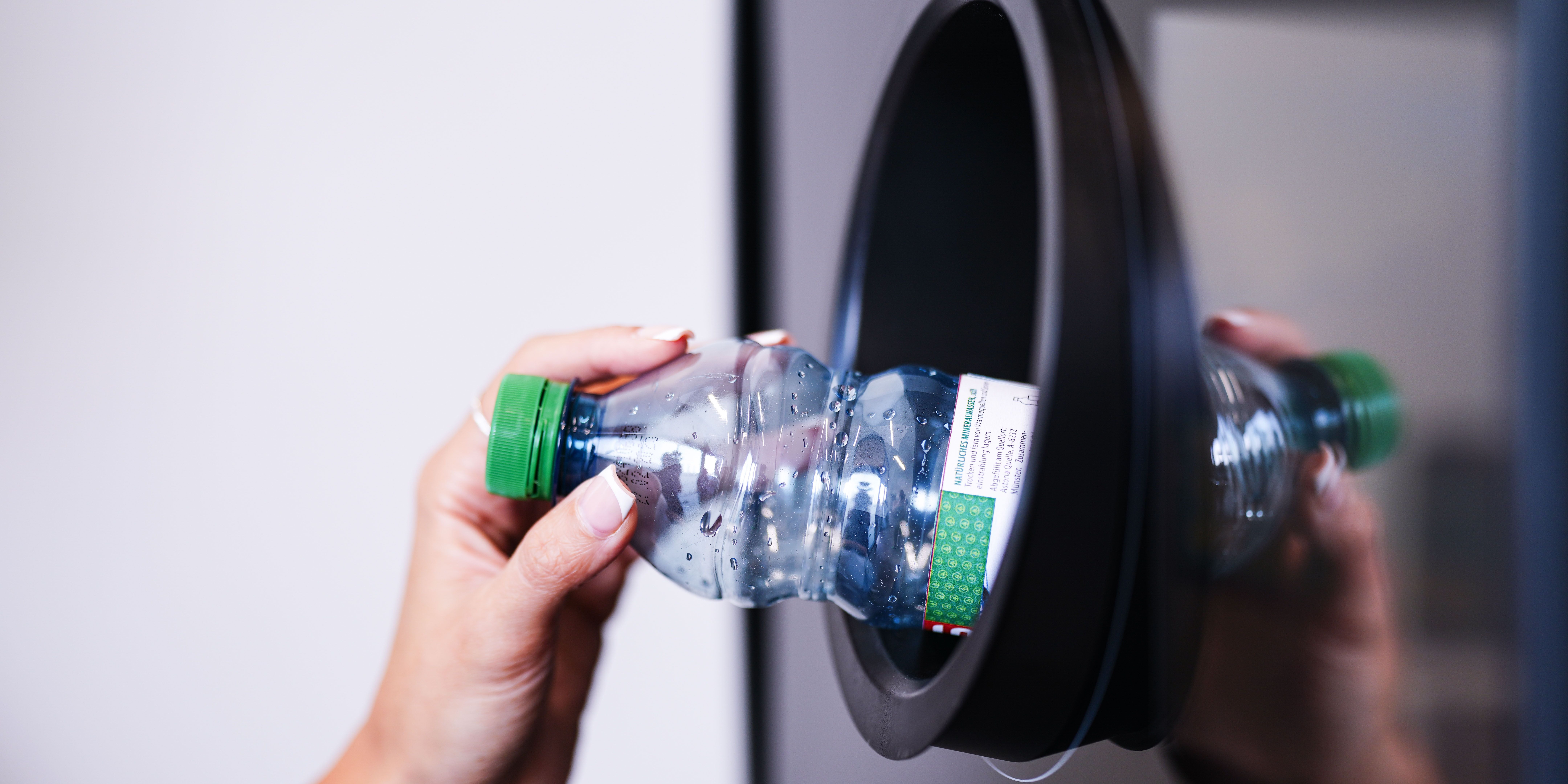 Eine Hand steckt eine leere Plastikflasche in einen Pfandautomaten.