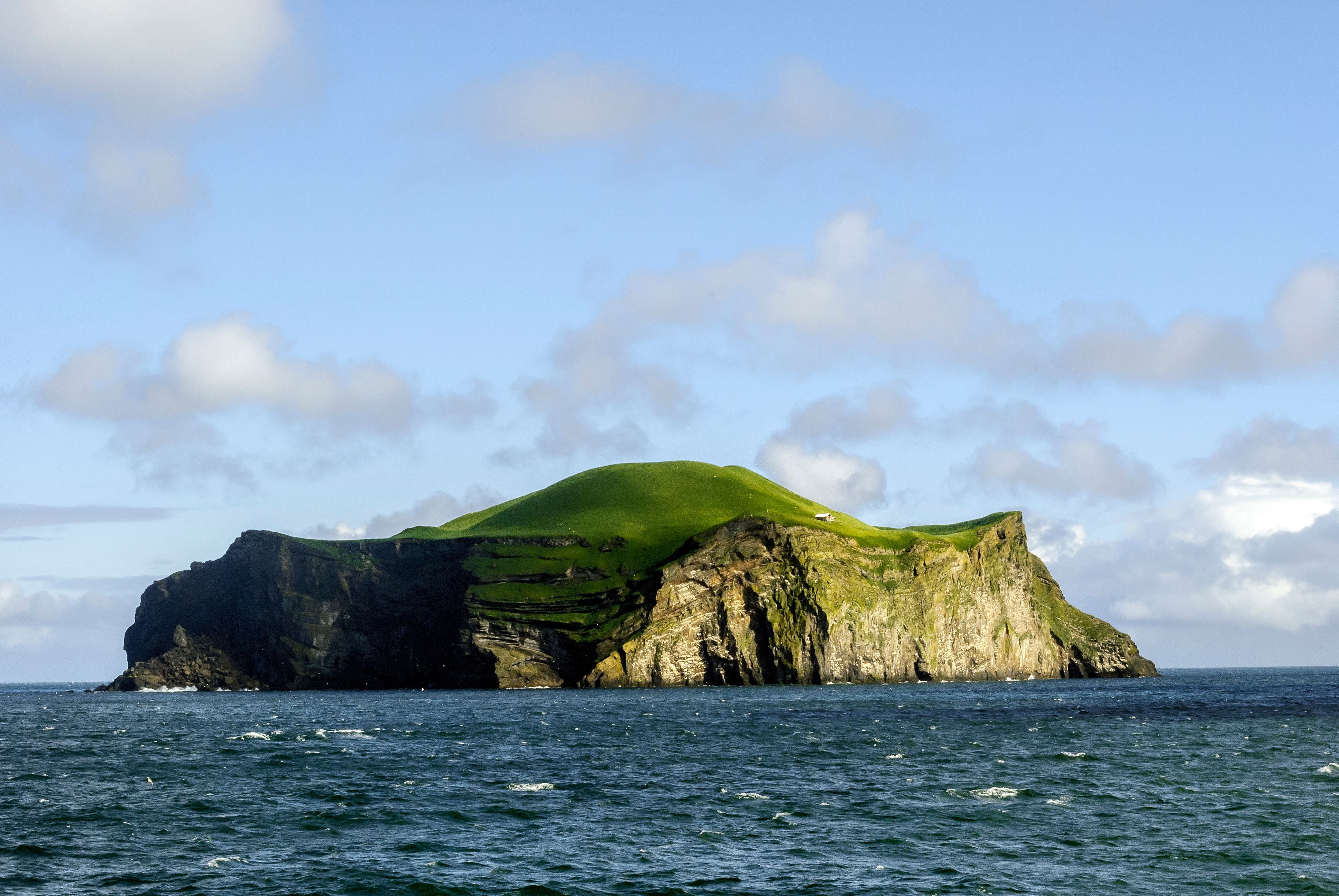 Grüne Insel mit einer einzelnen weißen Hütte auf einem Felsen im Meer.