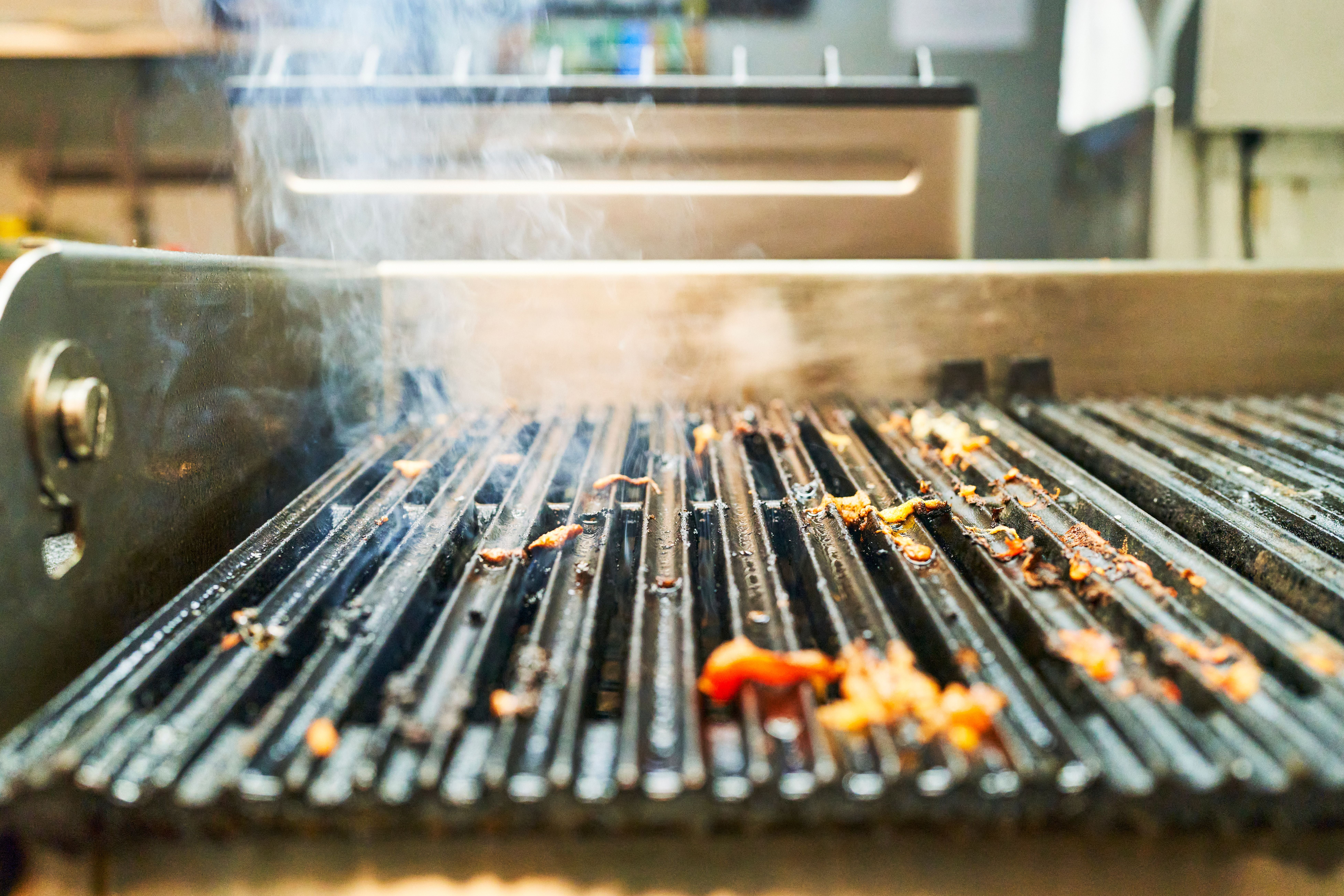 Nahaufnahme eines leeren Grillrosts mit angebrannten Essensresten und aufsteigendem Rauch.