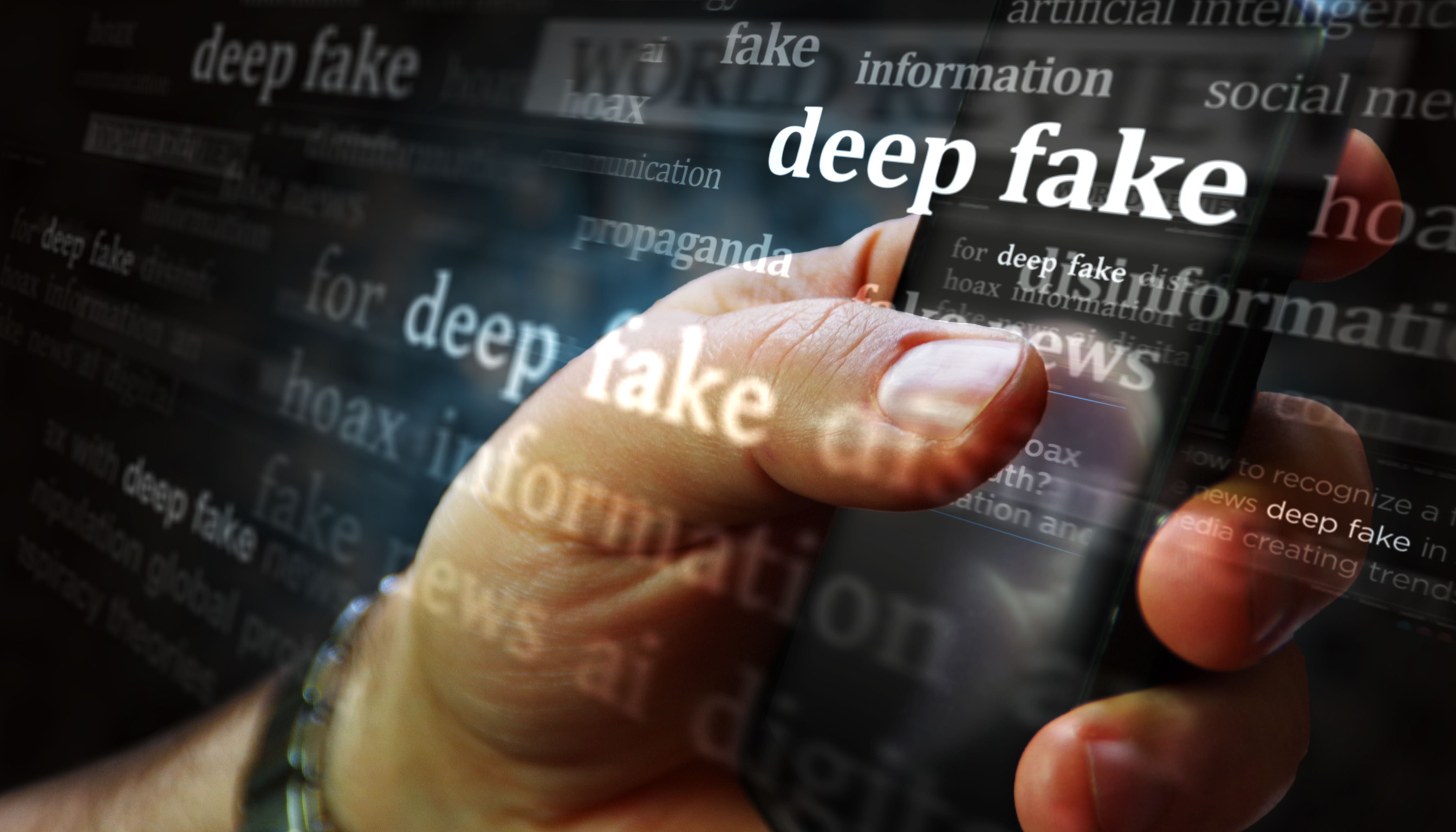 Hand hält Smartphone mit eingeblendetem Text „deep fake” und weiteren Schlagworten zum Thema.