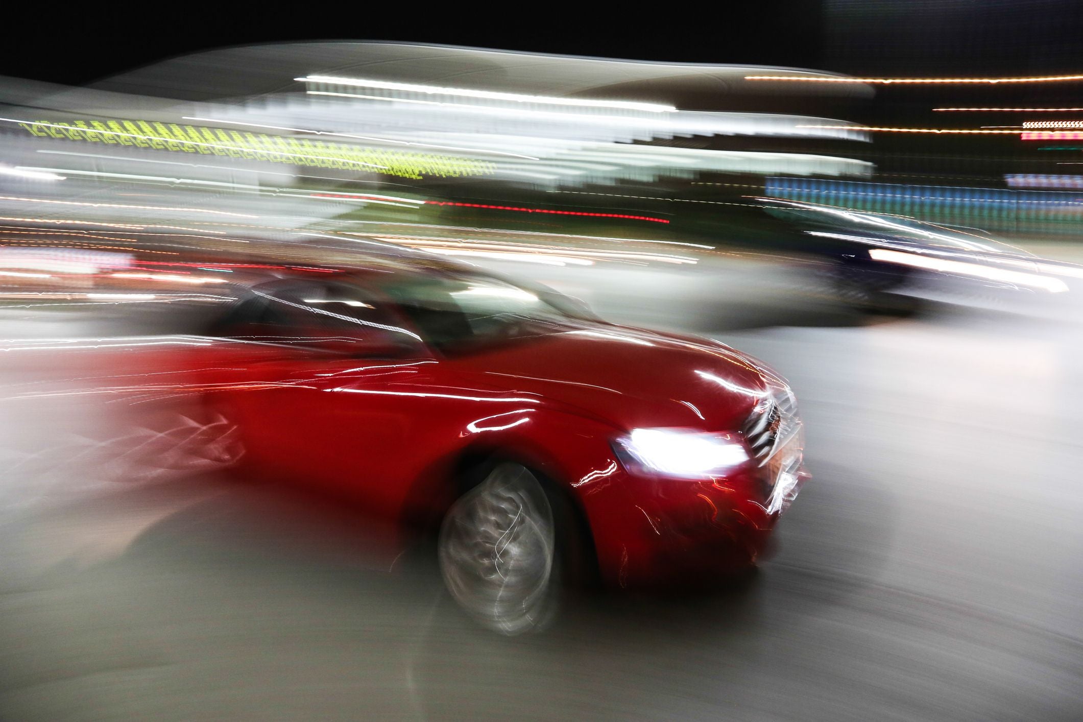 Rotes Auto fährt nachts mit Bewegungsunschärfe durch die Stadt.