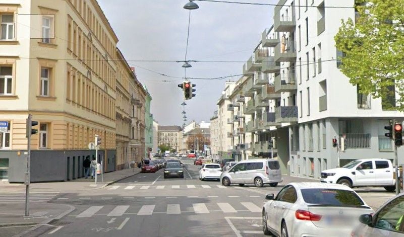 Straßenkreuzung in einer Stadt mit Autos, Ampeln und Wohngebäuden bei Tageslicht.