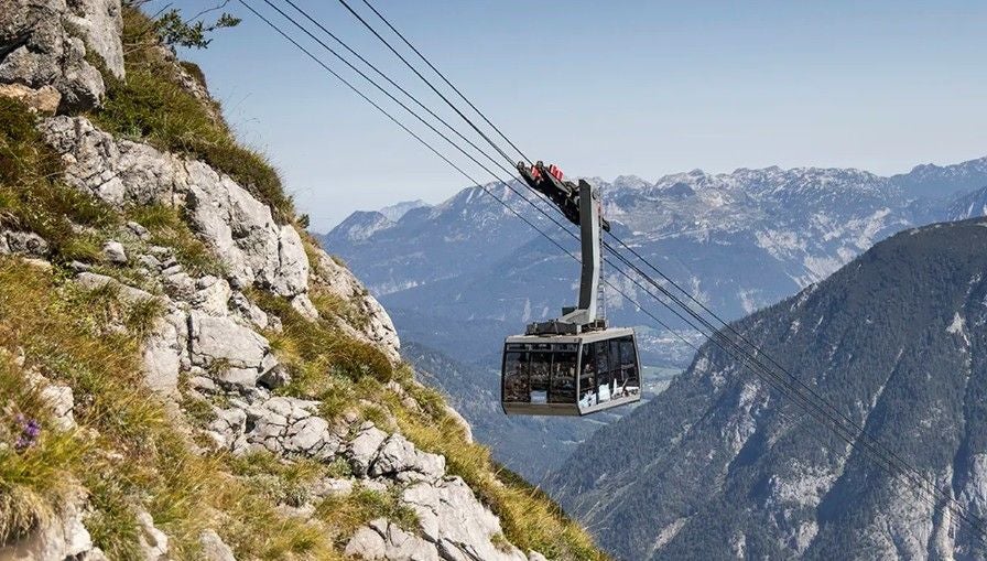 Eine Seilbahn fährt an steilen Felsen vorbei mit Berglandschaft im Hintergrund.