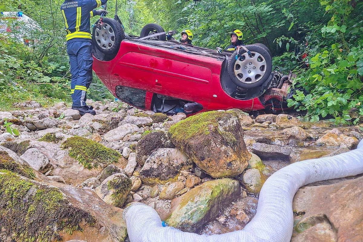 Feuerwehr sichert ein auf dem Dach liegendes rotes Auto im Wald, Rettungseinsatz läuft.