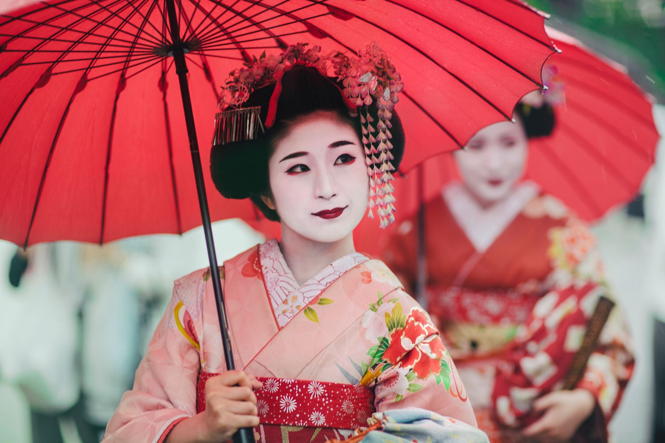 Maiko in Kimono mit traditionellem Make-up und rotem Regenschirm in Kyoto, Japan.