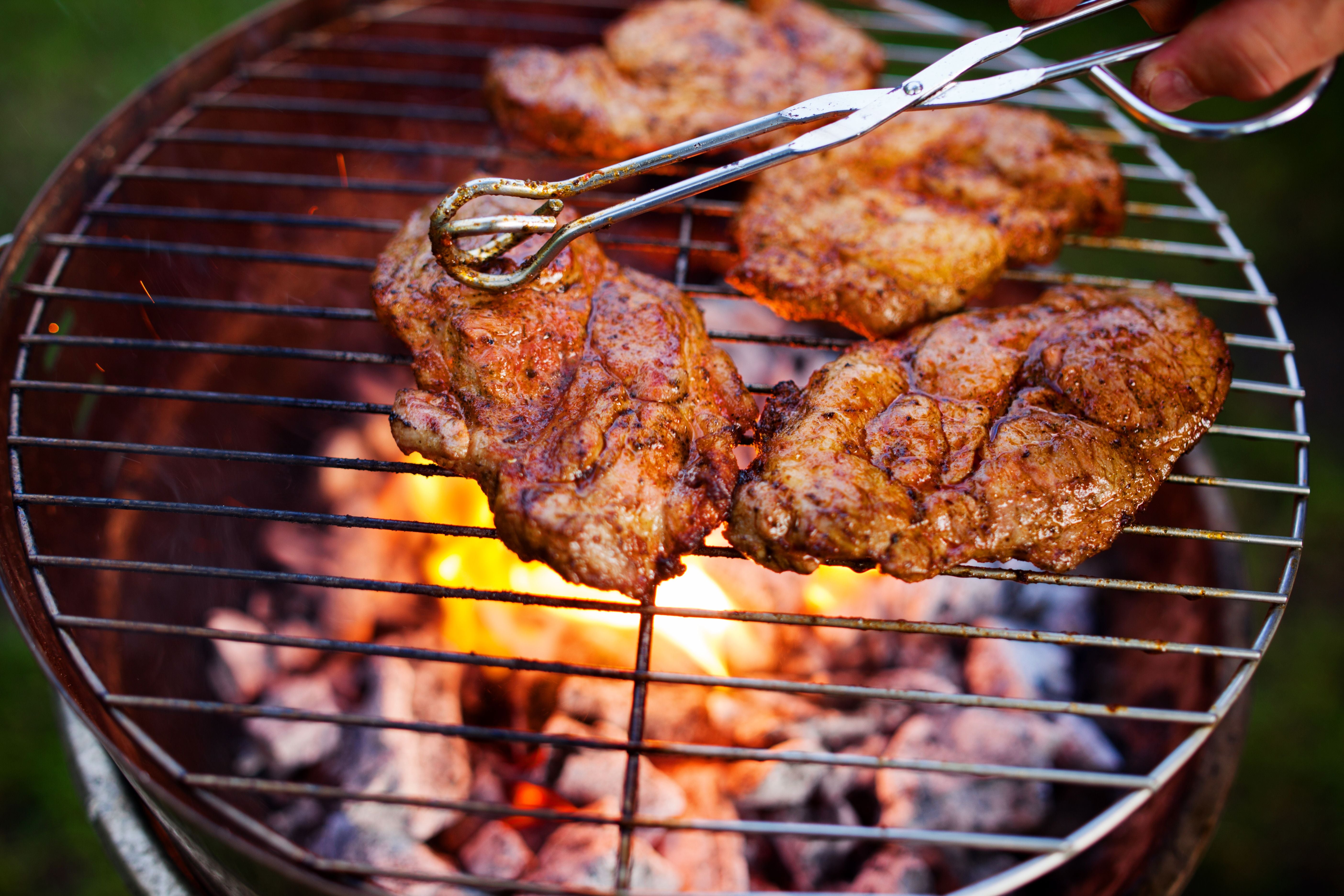 Nahaufnahme von Steaks auf einem Grill über offenen Flammen.