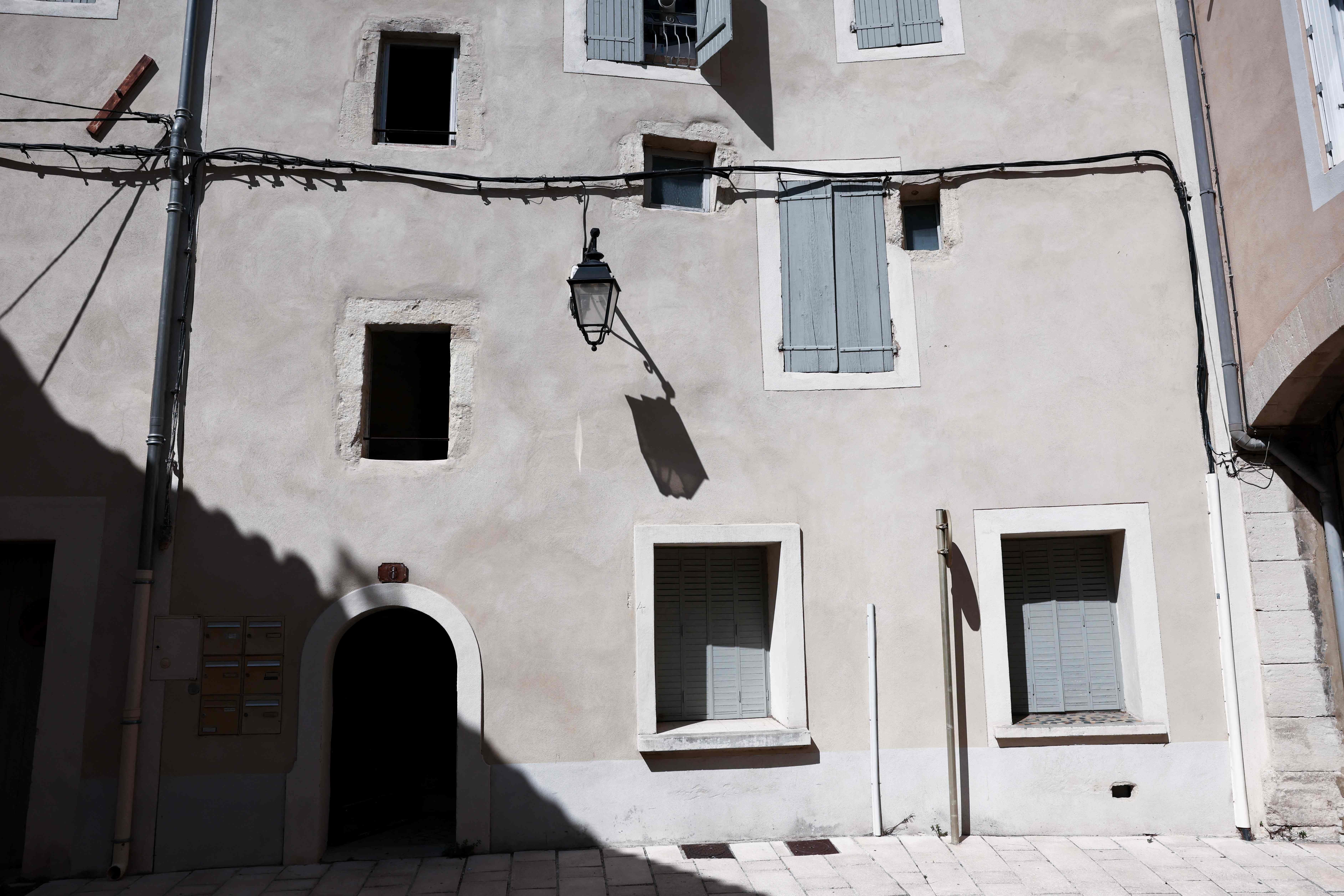 Eingang eines Wohnhauses mit geschlossenen Fensterläden und einer Straßenlaterne an der Fassade.