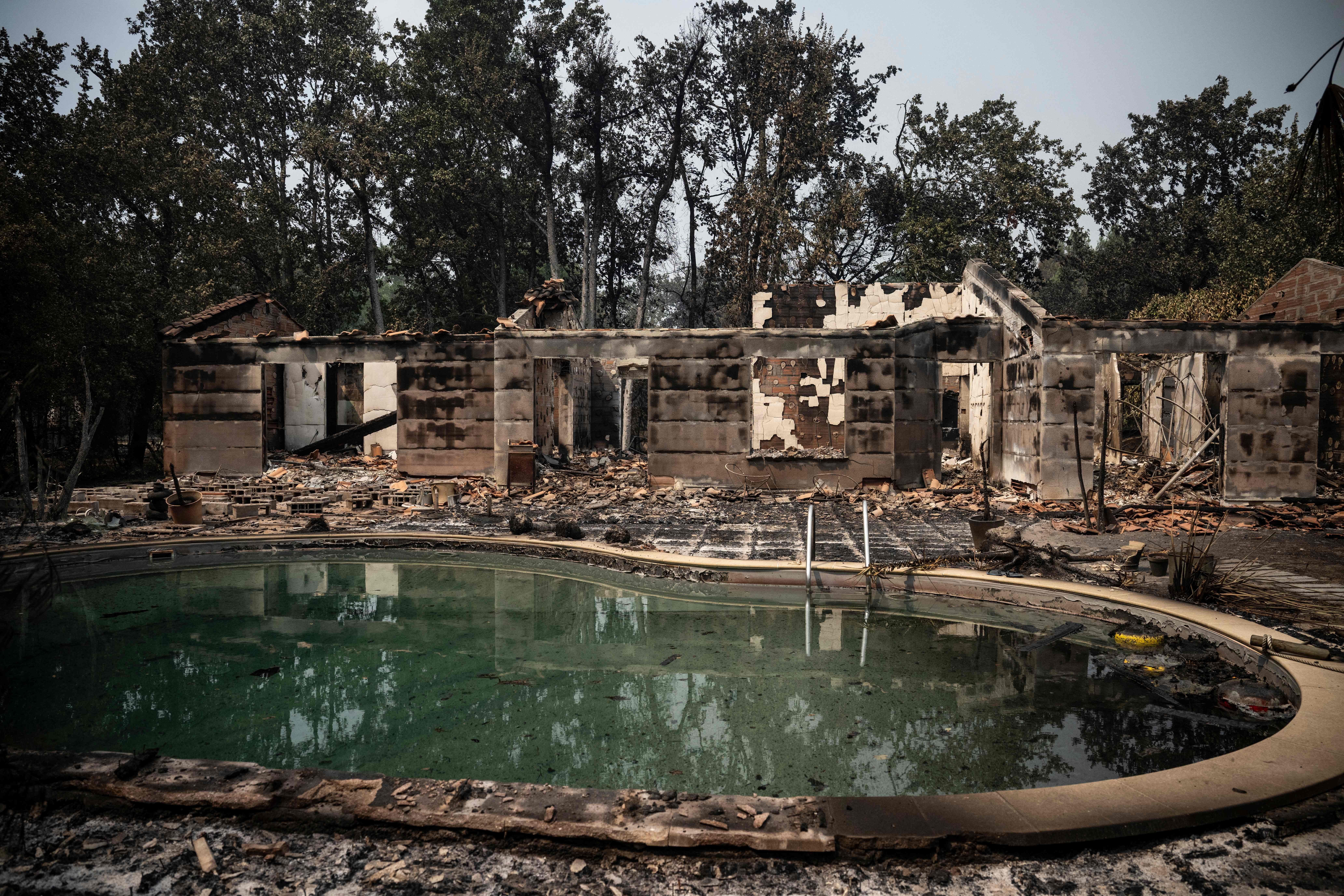 Verbranntes Haus und zerstörte Umgebung mit einem schmutzigen Pool nach einem Waldbrand.